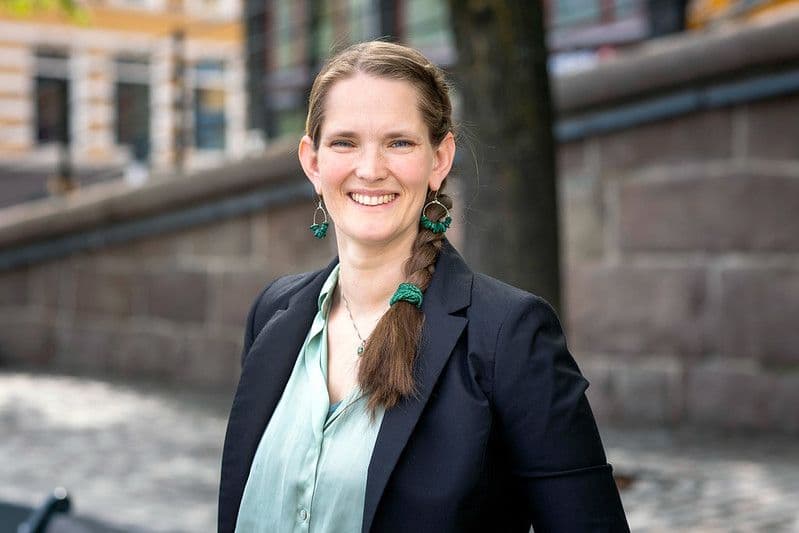 Smilende kvinne med flettefrisyre, grønne øredobber og svart blazer.