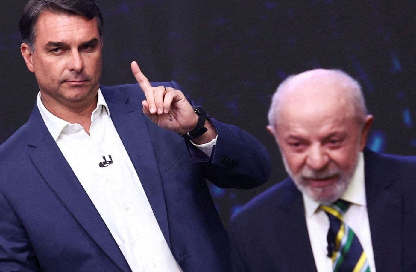 Fernando Francischini points with a serious expression as Lula da Silva looks distressed and blurry in the background.