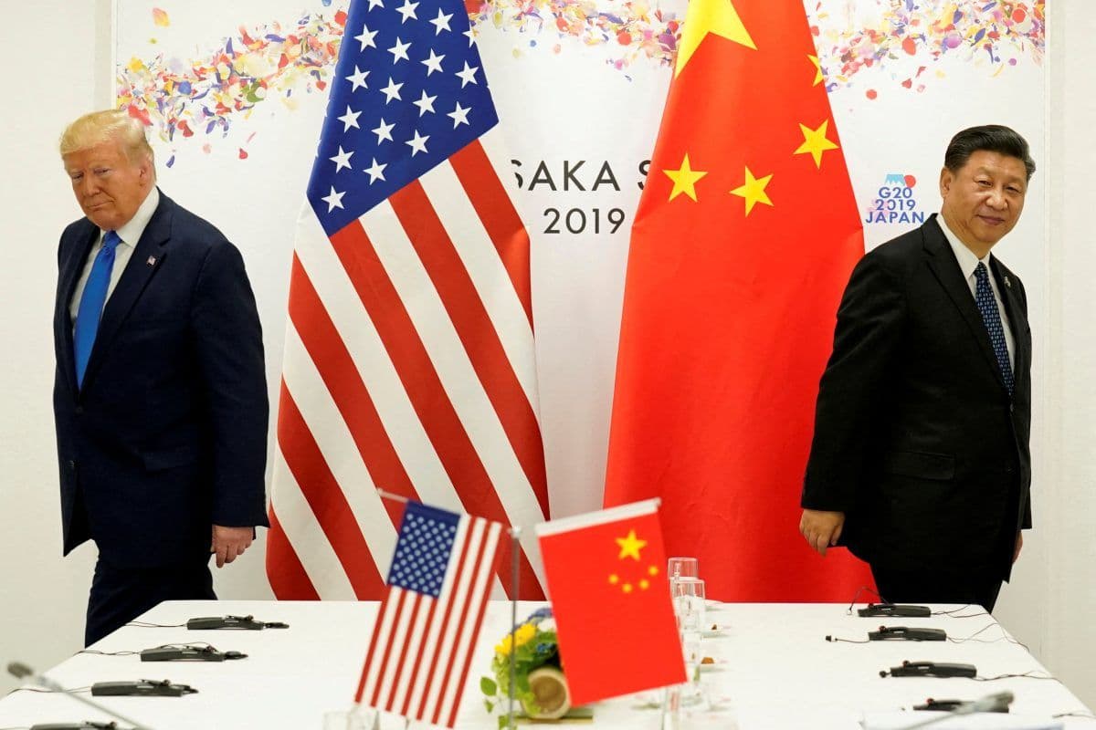 To menn går i hver sin retning foran store amerikanske og kinesiske flagg ved et formelt møtebord, med G20 Japan 2019-skilt i bakgrunnen.