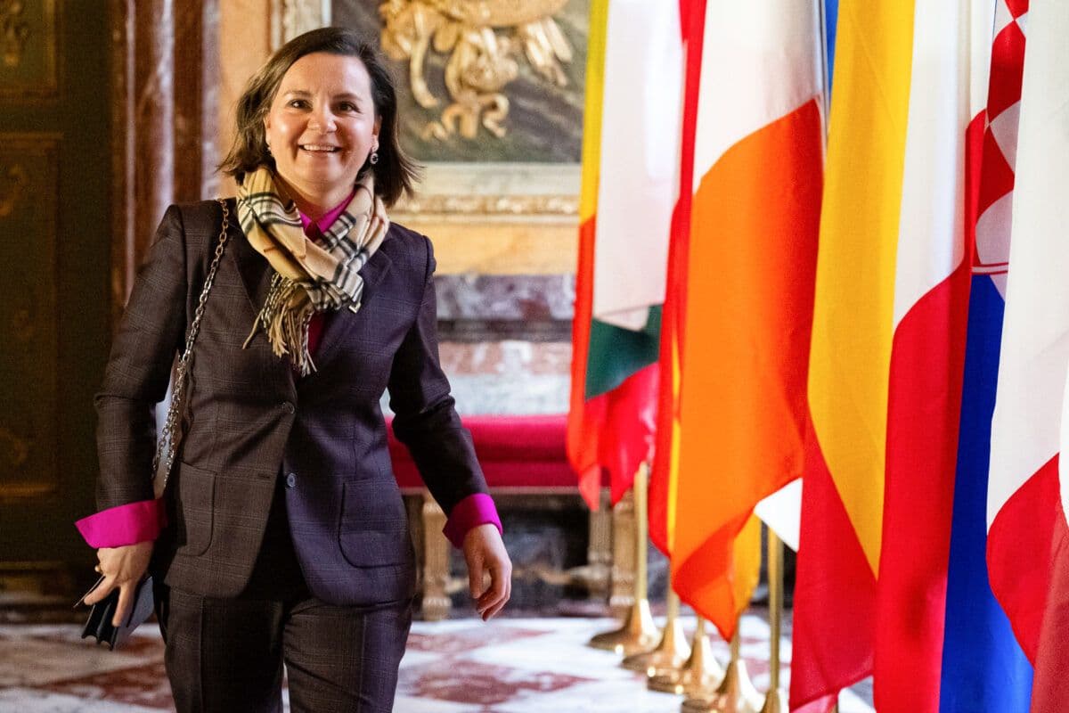 En kvinne i dress som står foran flagg.