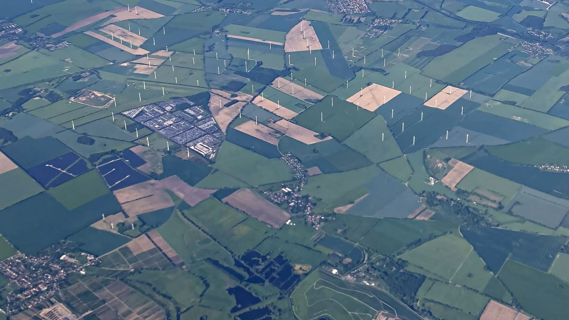 Flyfoto av et landskap med en rekke vindturbiner, solparker, jordbruksarealer og et industriområde.