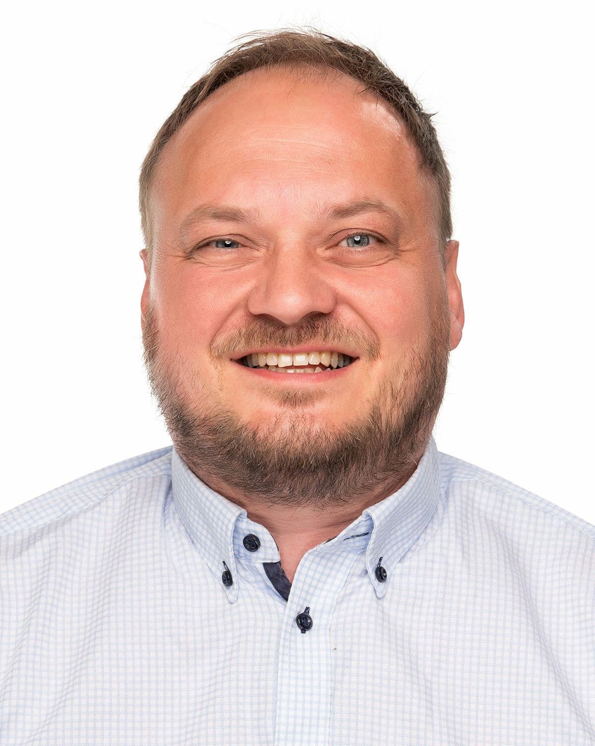 Smilende mann med skjeggstubb og lyseblå rutete skjorte.