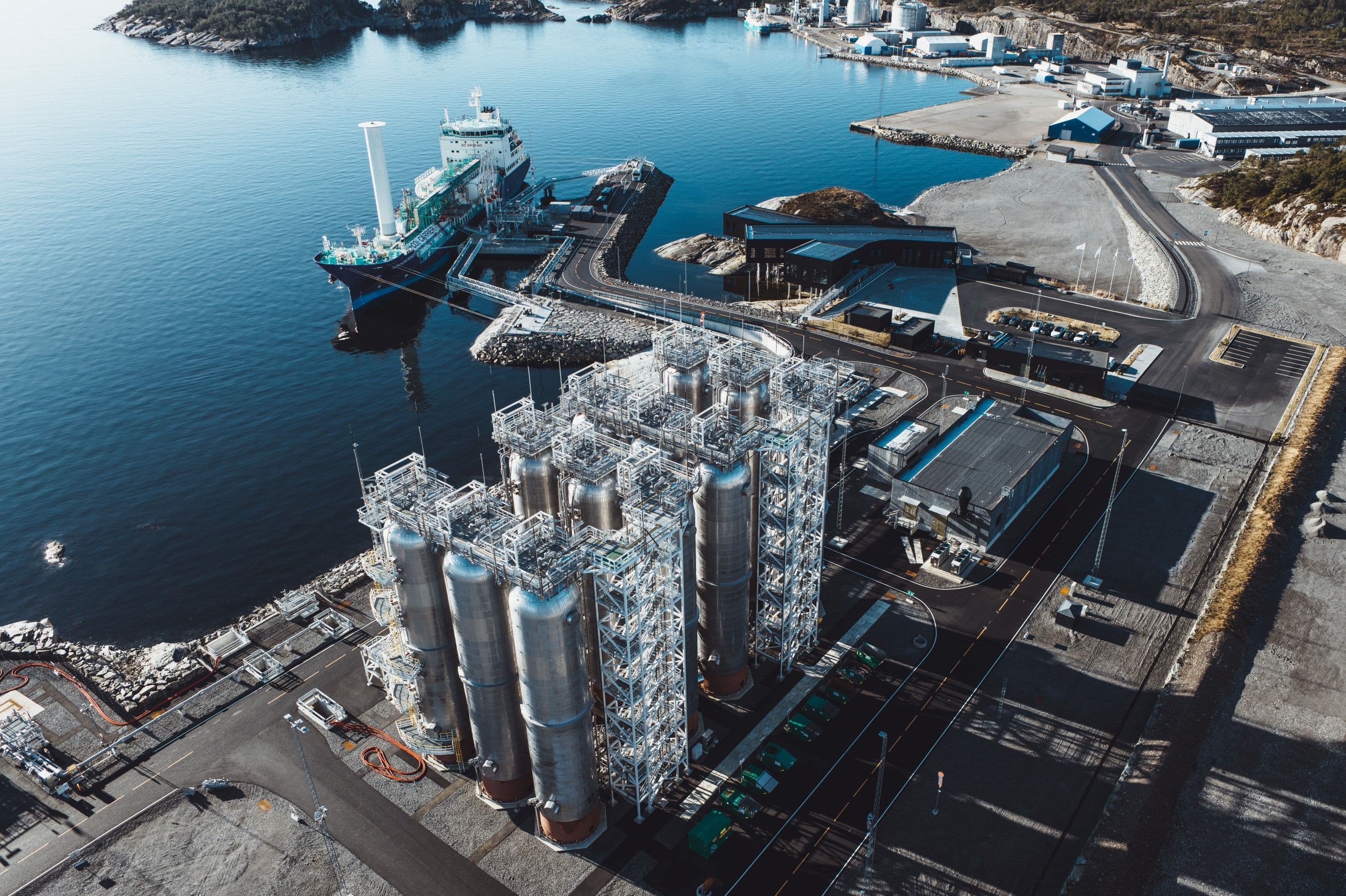Tankskip fortøyd ved et kystnært industrianlegg med store lagertanker.