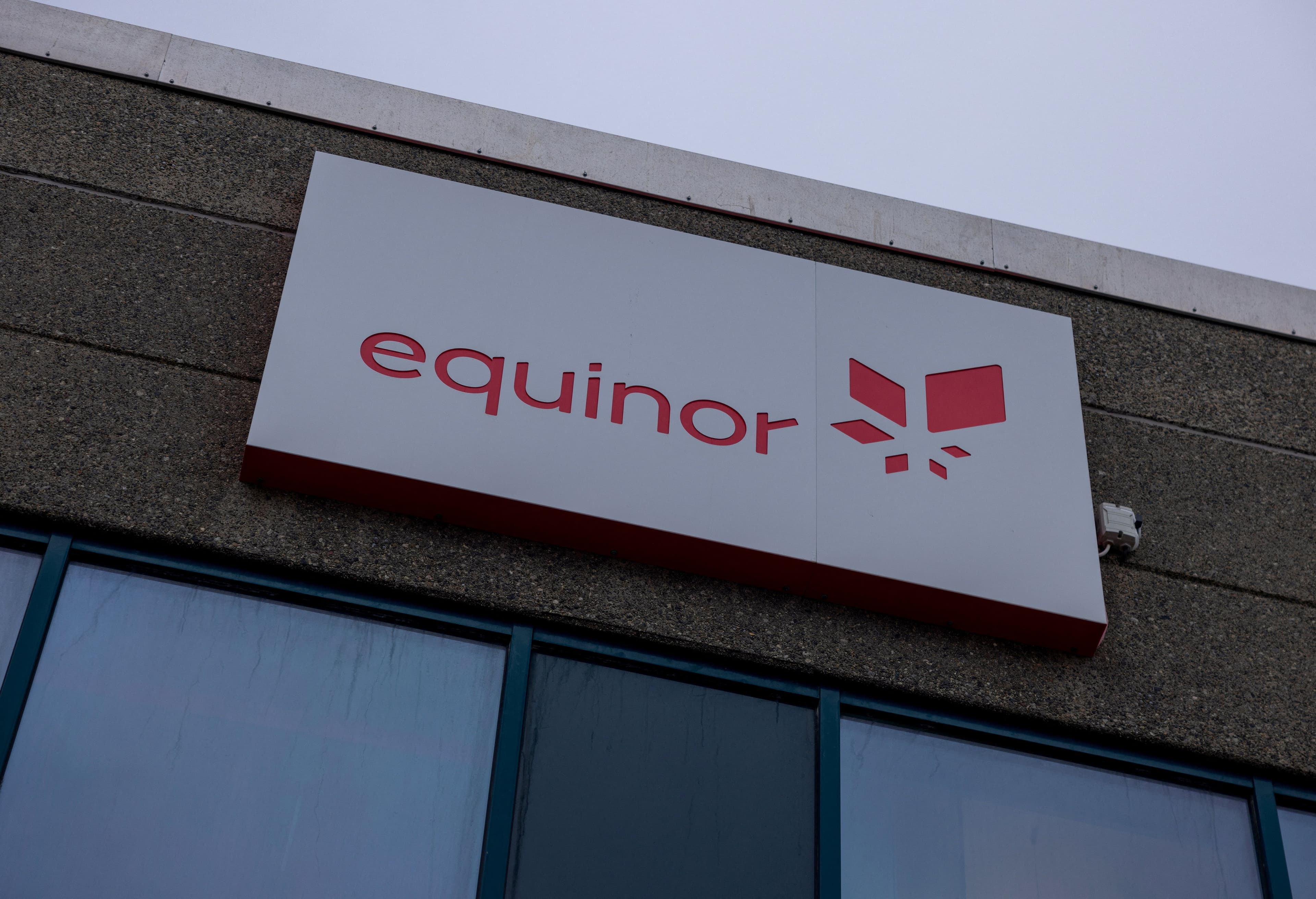 Et Equinor-skilt med rød «Equinor»-tekst og logo på hvit bakgrunn, montert på en grå bygning.