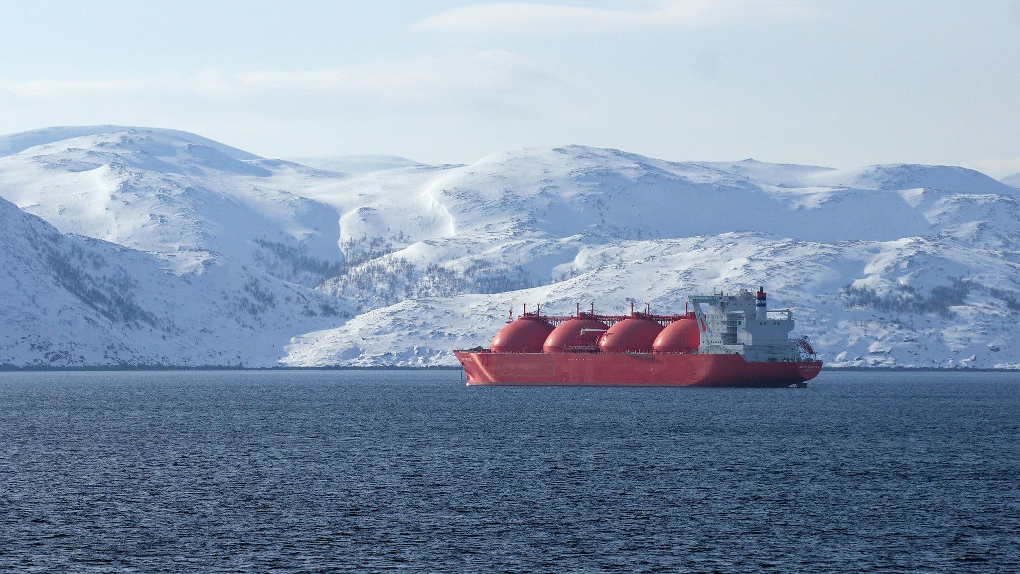 Rødt LNG-skip seiler forbi snødekte fjell.