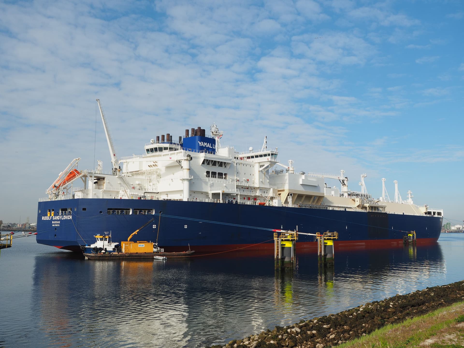 En stor blå og hvit LNG-tanker, «Fedor Litvinov», ligger til kai i en rolig havn under en delvis skyet himmel.