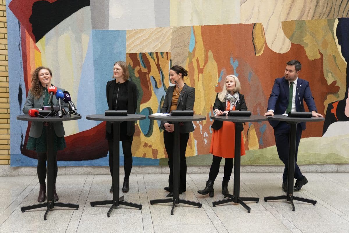 Fem personer står bak podier foran en fargerik, abstrakt vegg og deltar i det som ser ut til å være en pressekonferanse eller paneldiskusjon.