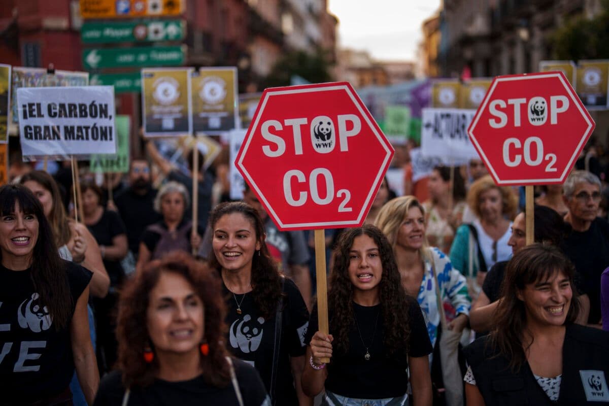 Demonstranter bærer "stopp co2"-skilt ved en demonstrasjon av klimaendringer, med mennesker i forskjellige aldre som smiler og går i en bygate.
