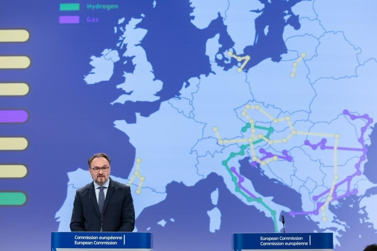 En mann taler fra en talerstol tilhørende EU-kommisjonen, med et kart over Europa bak seg som viser rørledningsnett for hydrogen (grønt) og gass (lilla).
