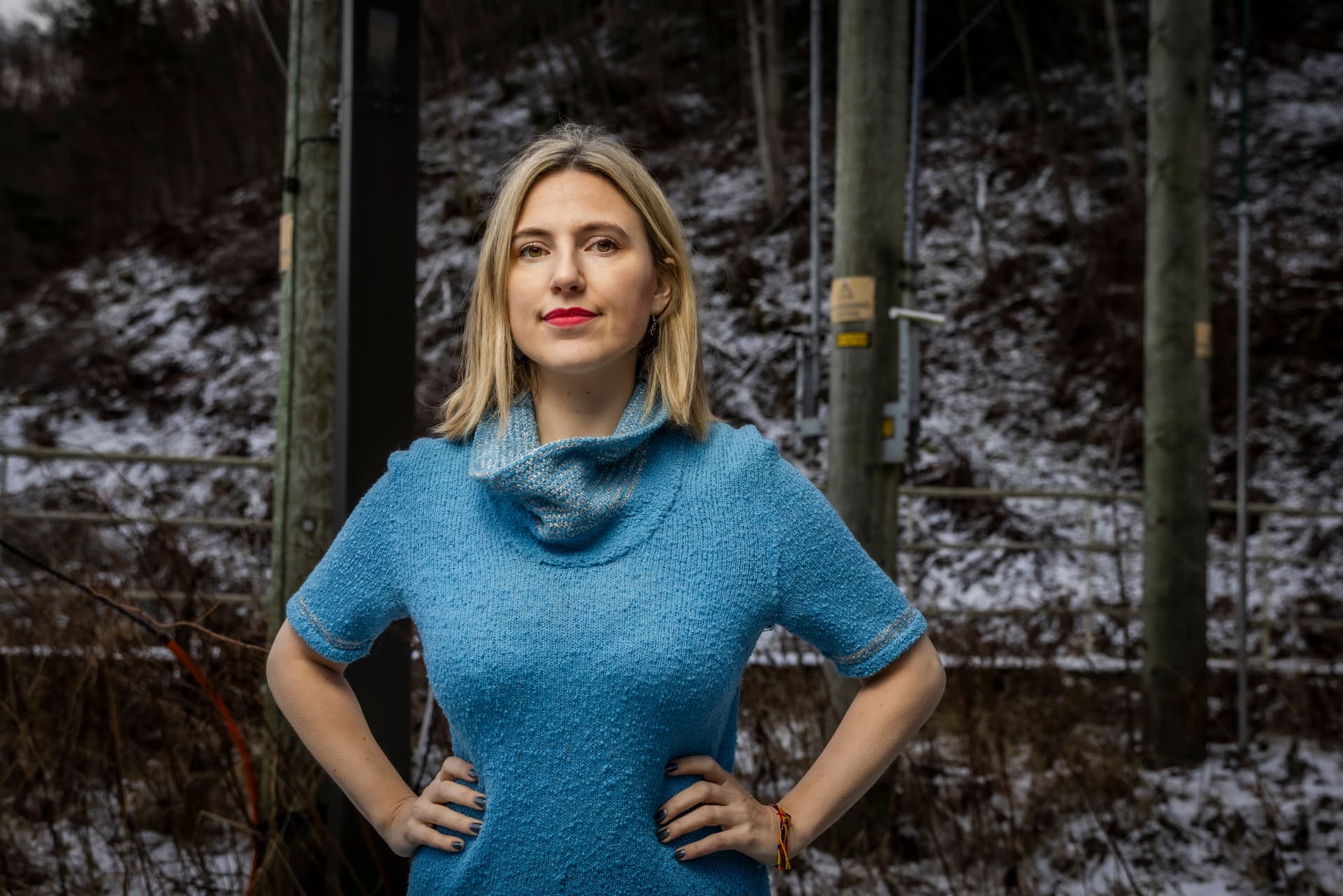 Bildet viser Sofie Marhaug i blå genser som står med hendene i siden i et snødekt skoglandskap med strømstolper.