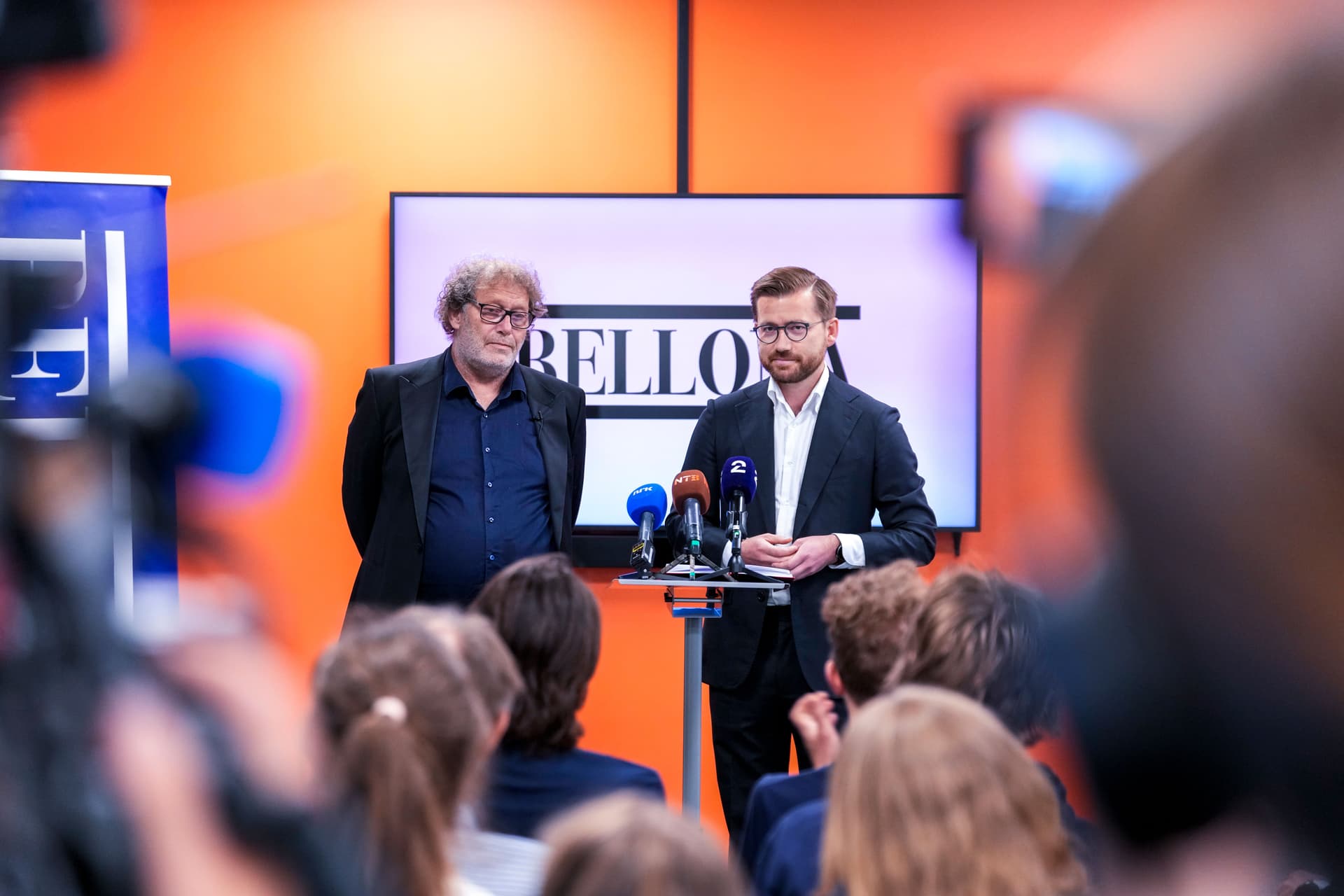 To menn, den ene taler fra en talerstol med mikrofoner, henvender seg til publikum på en pressekonferanse.