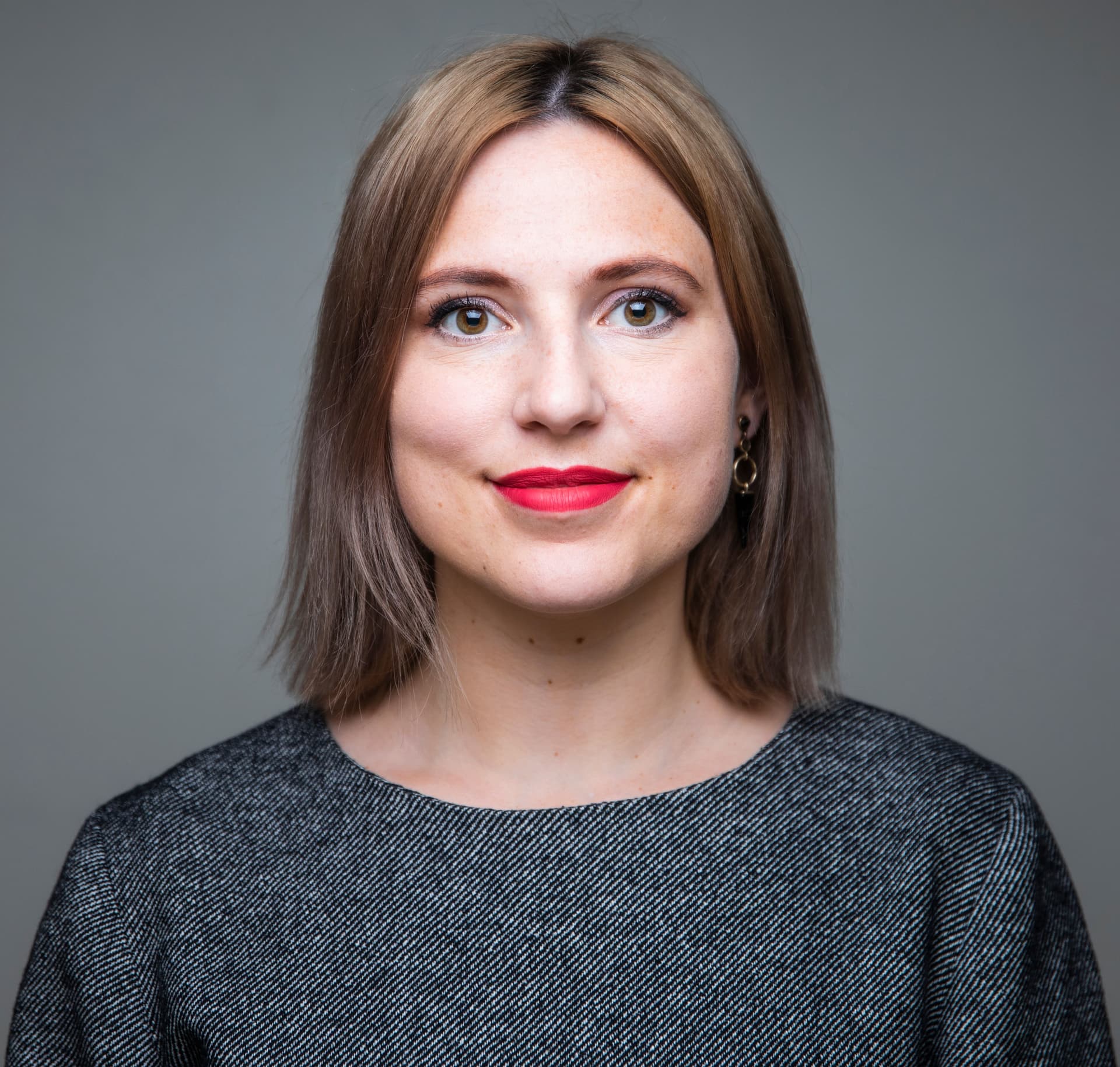 Headshot of a woman with light brown hair, red lipstick, and a slight smile.