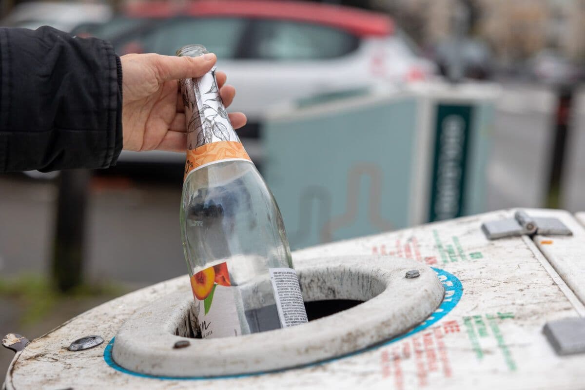 En person legger en flaske i en søppelbøtte.