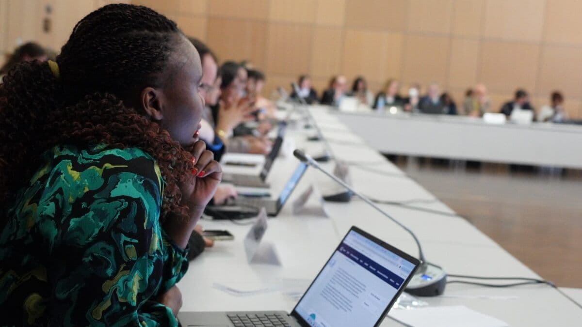 Folk sitter ved et langt konferansebord og fokuserer på diskusjoner og jobber med bærbare datamaskiner.