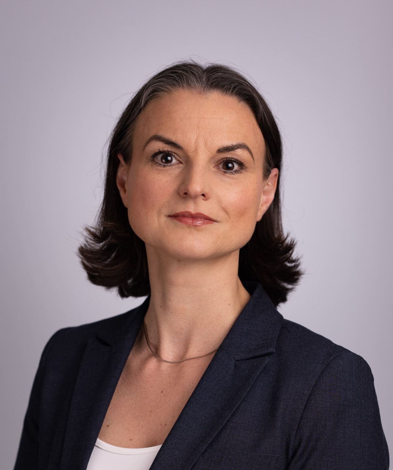 Profesjonelt portrett av en kvinne med mørkt hår som har på seg en mørk blazer.