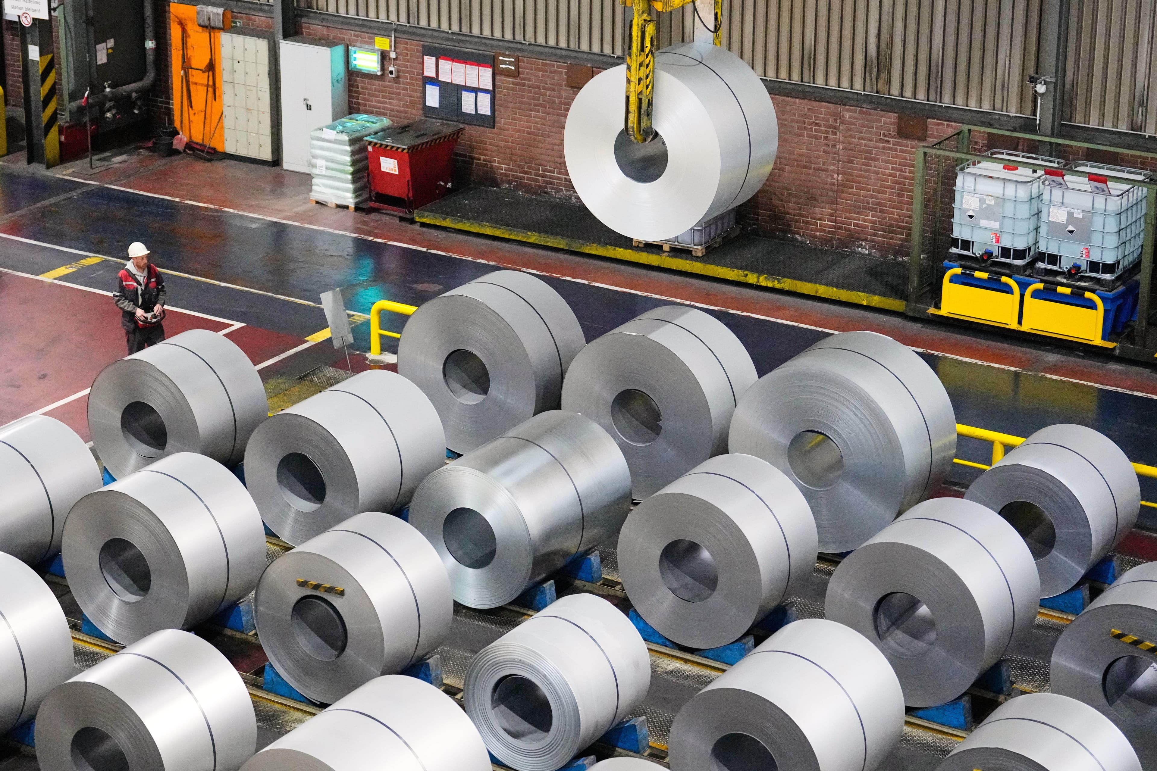 Large coils of metal on a factory floor, with one being lifted by a crane.