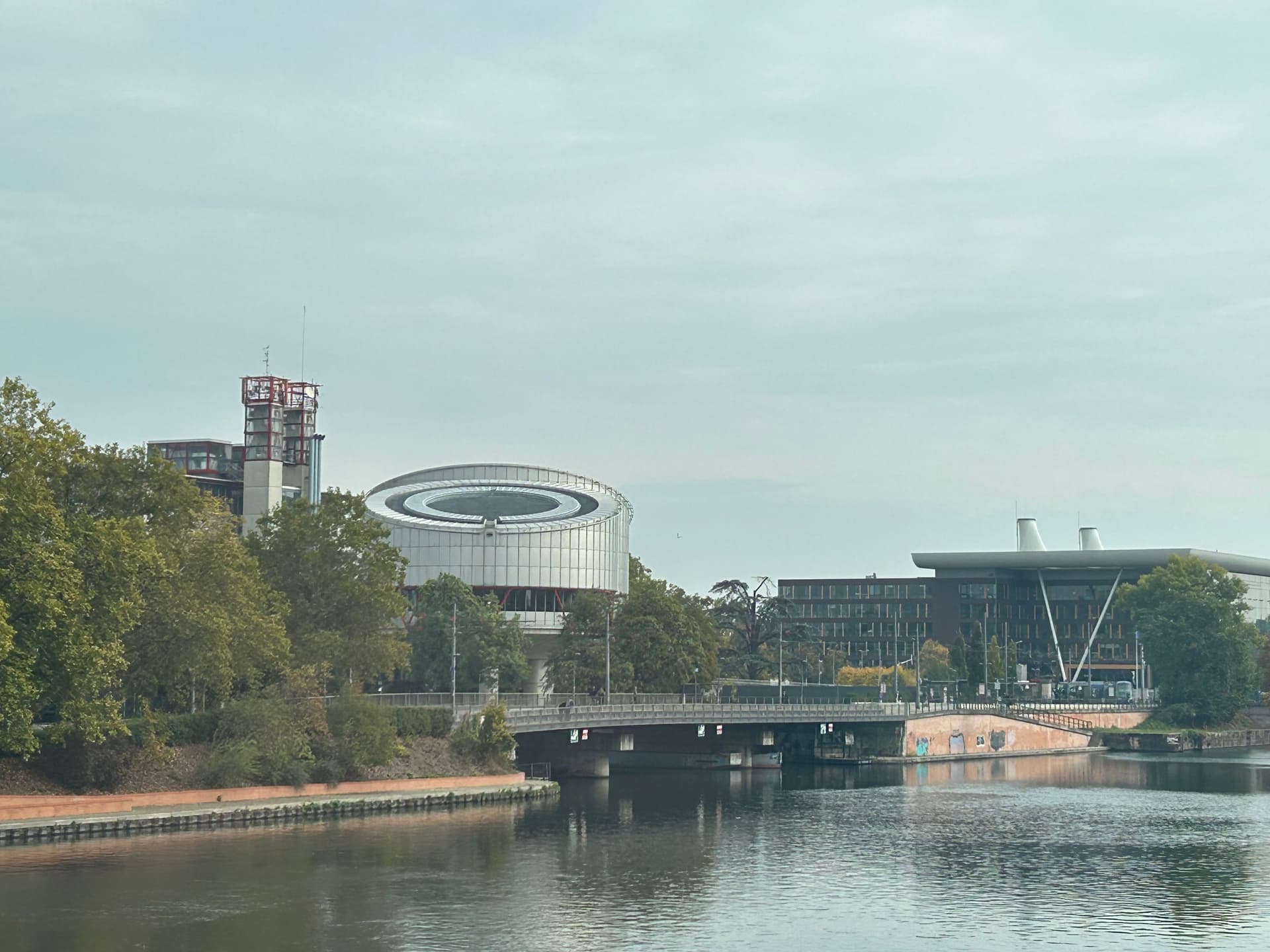 The European Court of Human Rights building and other modern structures along a river under a cloudy sky.