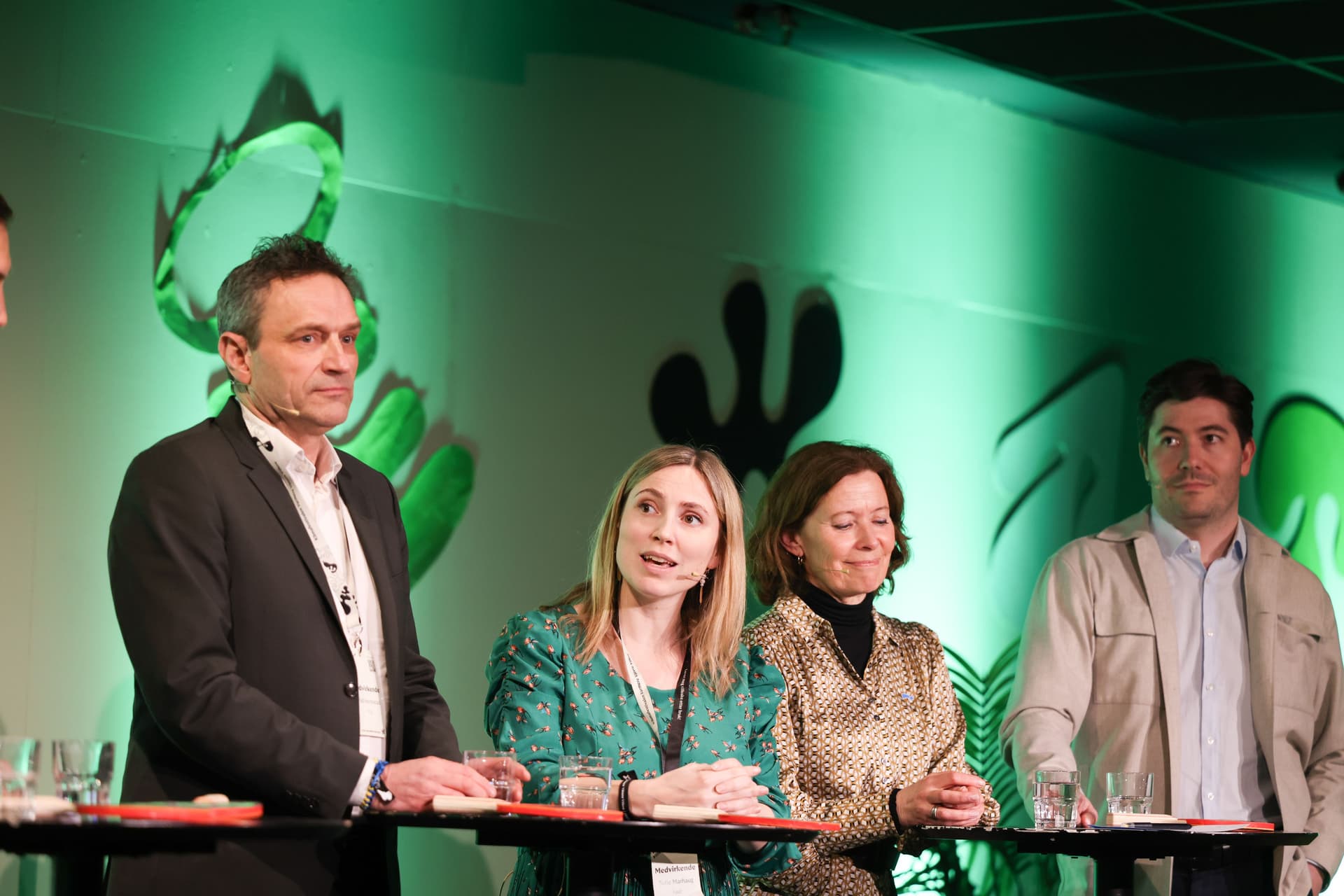 Fire personer i en paneldebatt, en kvinne snakker i en mikrofon.