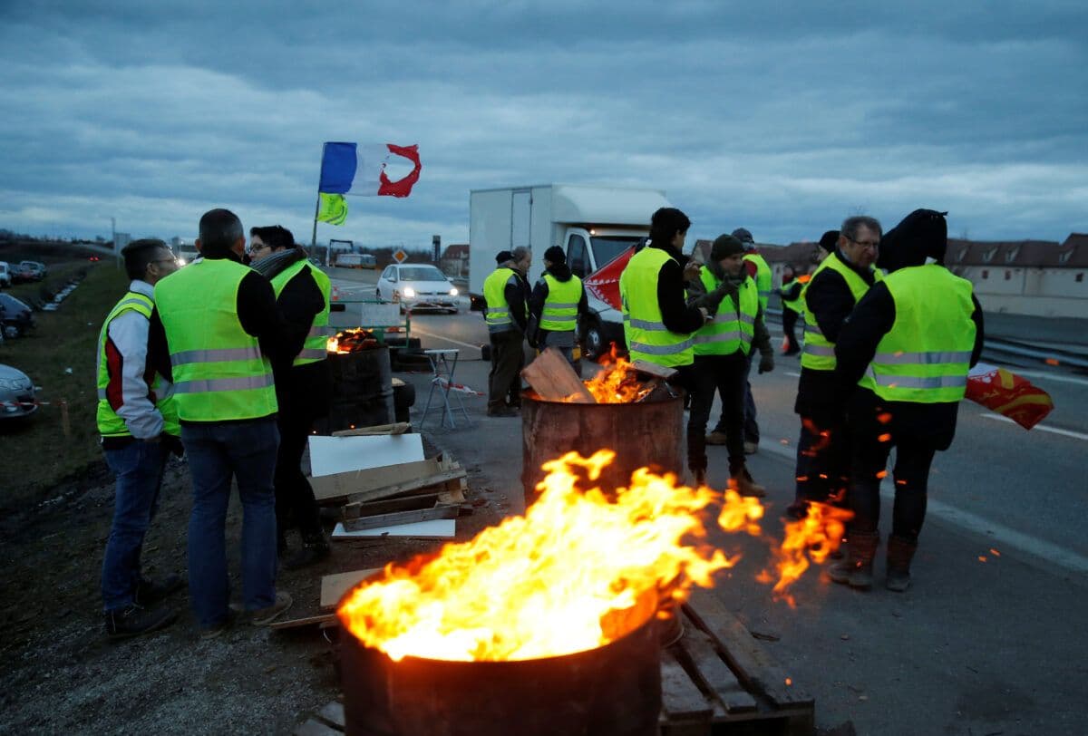 En gruppe mennesker i gule vester som står rundt oljetønner som brenner.