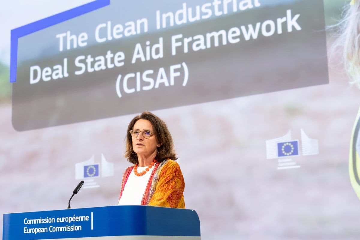 En kvinne står på et podium merket "EU-kommisjonen" og snakker foran en skjerm som viser "The Clean Industrial Deal State Aid Framework (CISAF)".
