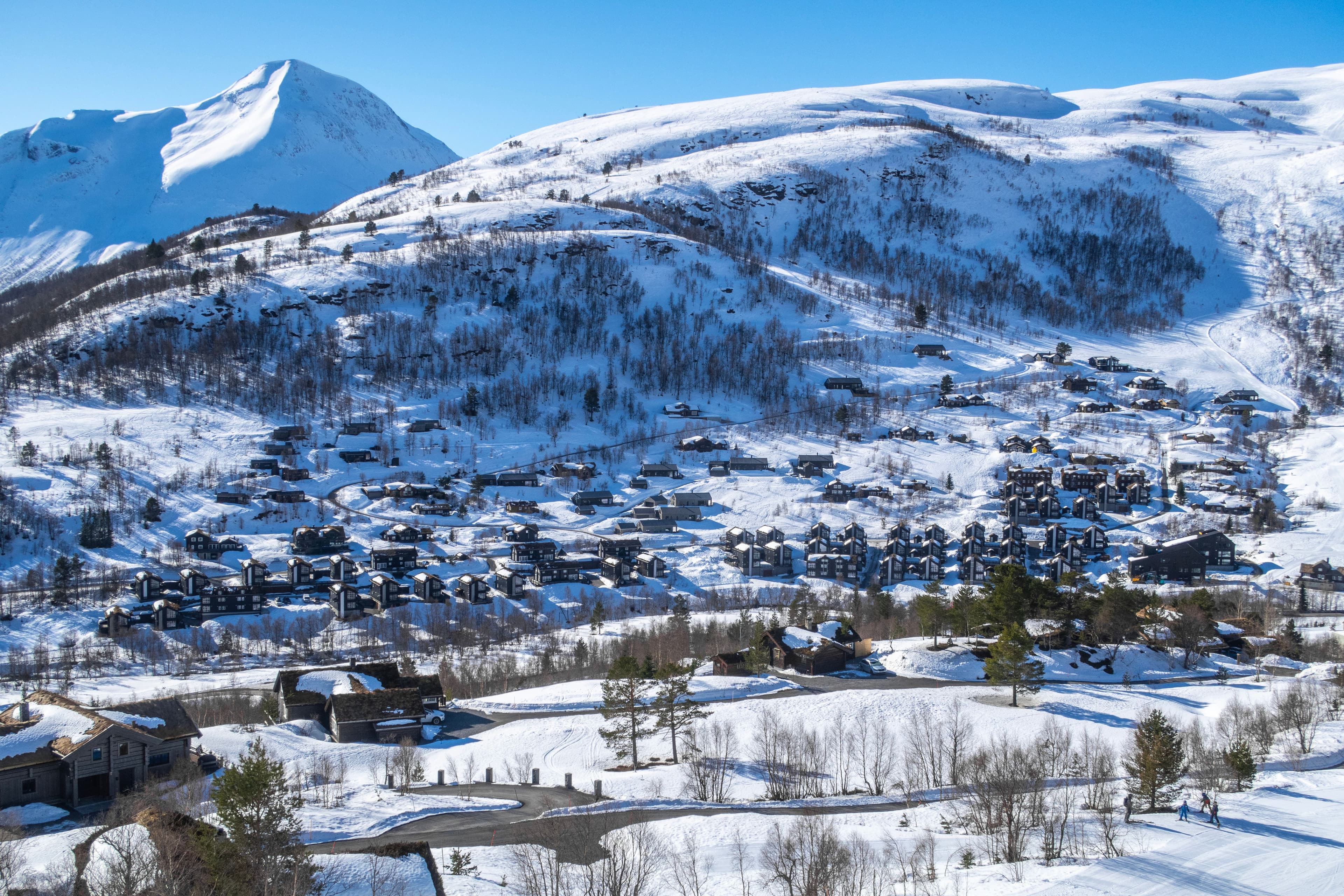 En snødekt landsby som ligger i en fjelldal under en klar blå himmel.