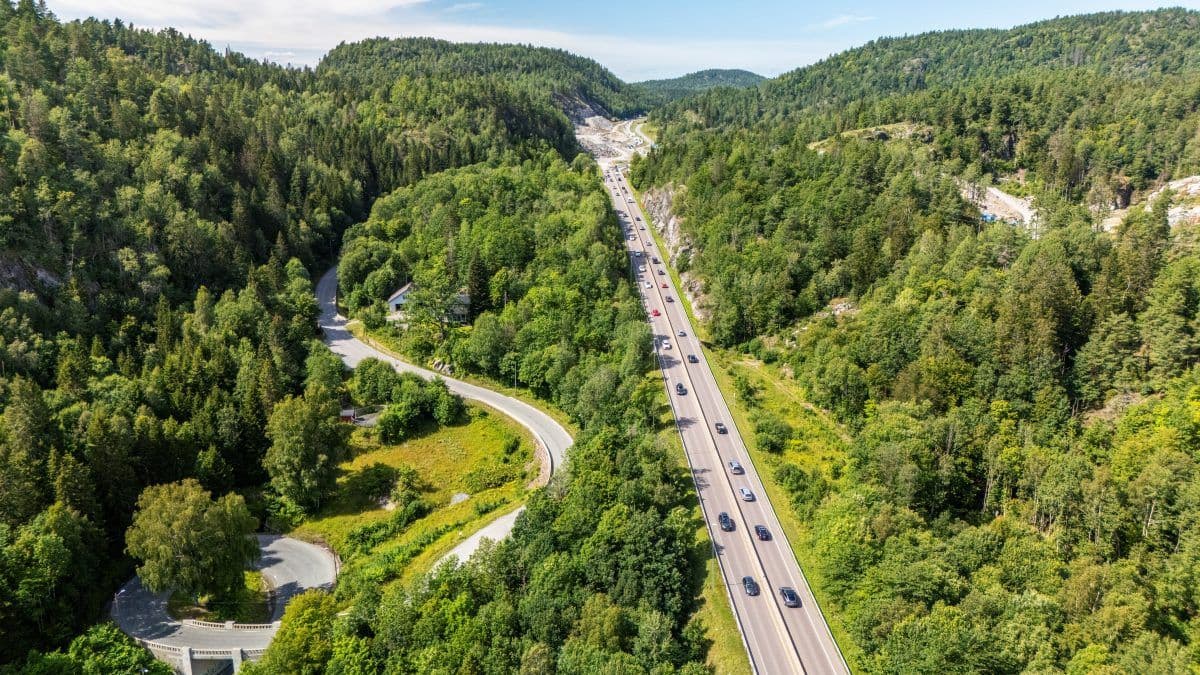 Luftfoto av en motorvei med biler som kjører gjennom et grønt skogsområde på en solrik dag.