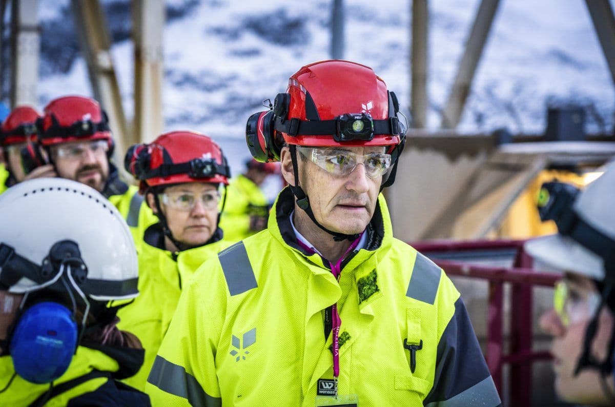 En gruppe arbeidere iført varselvester, hjelmer og vernebriller står sammen på et industriområde.
