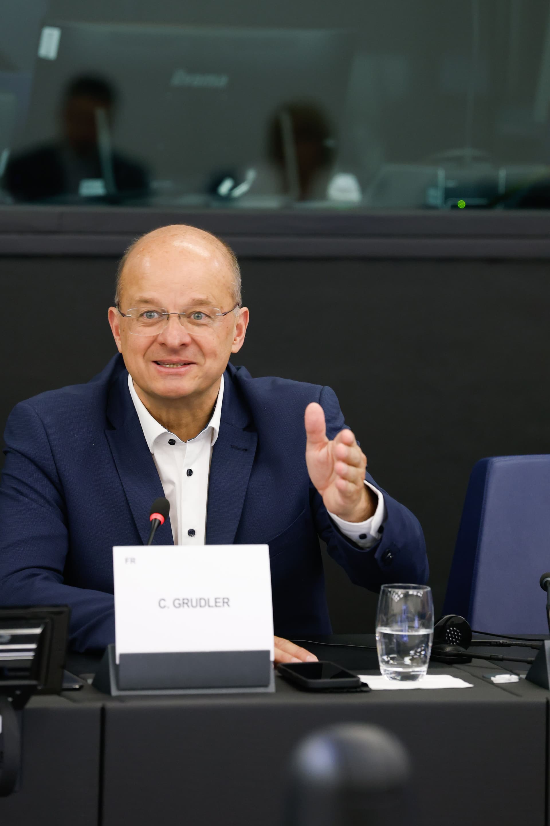 C. Grudler, a man in a blue suit and glasses, speaks and gestures at a table.