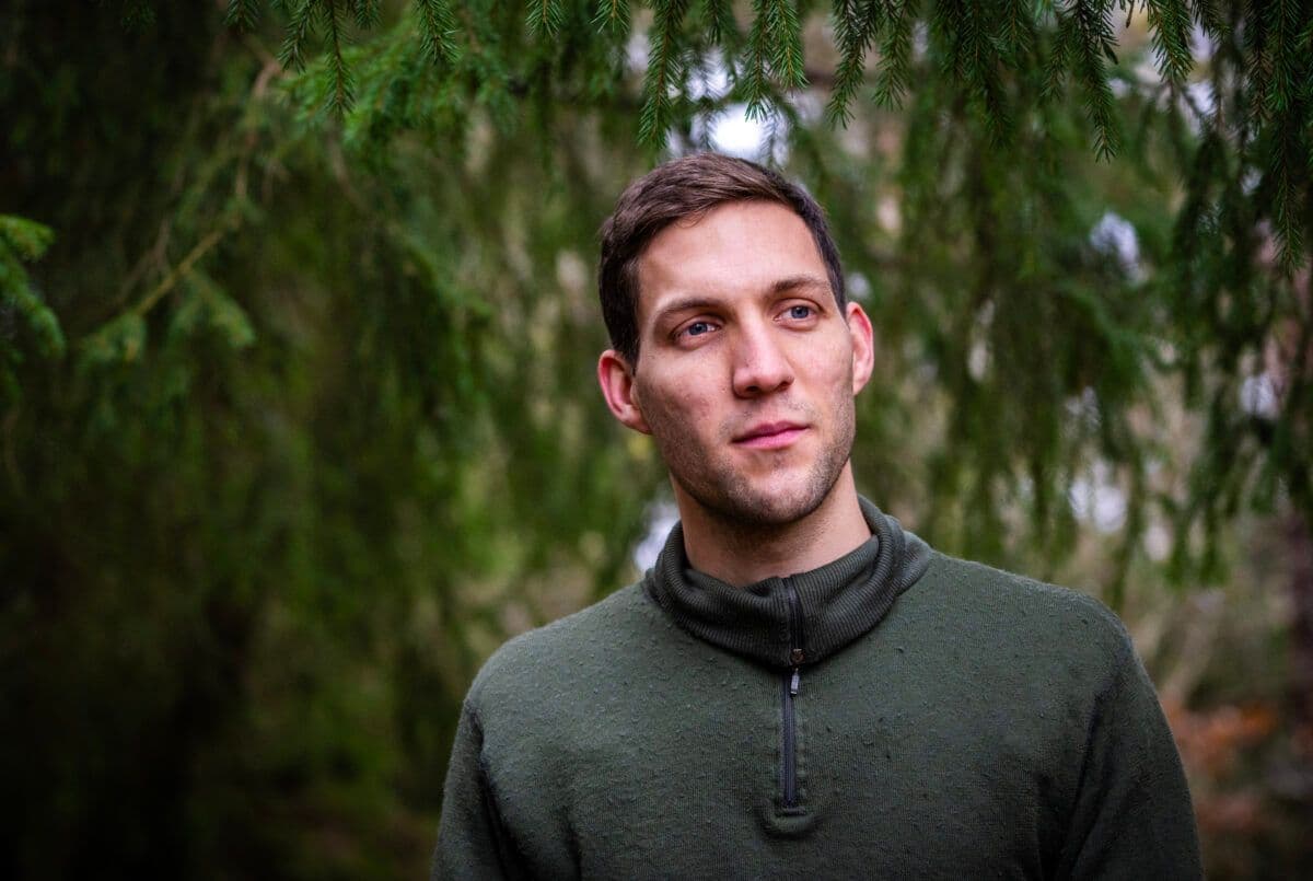 Mann i en grønn høyhalset genser stående i en skog.