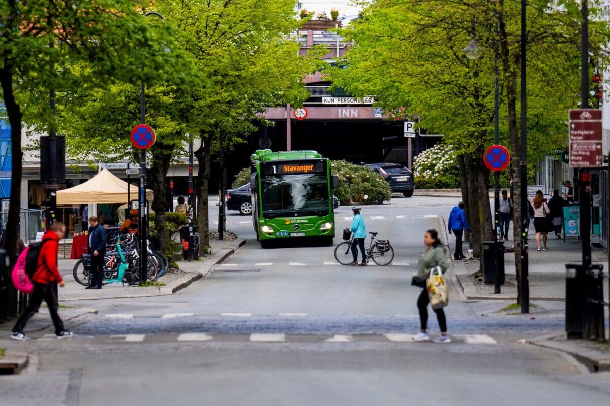 En grønn buss kjører nedover en bygate.