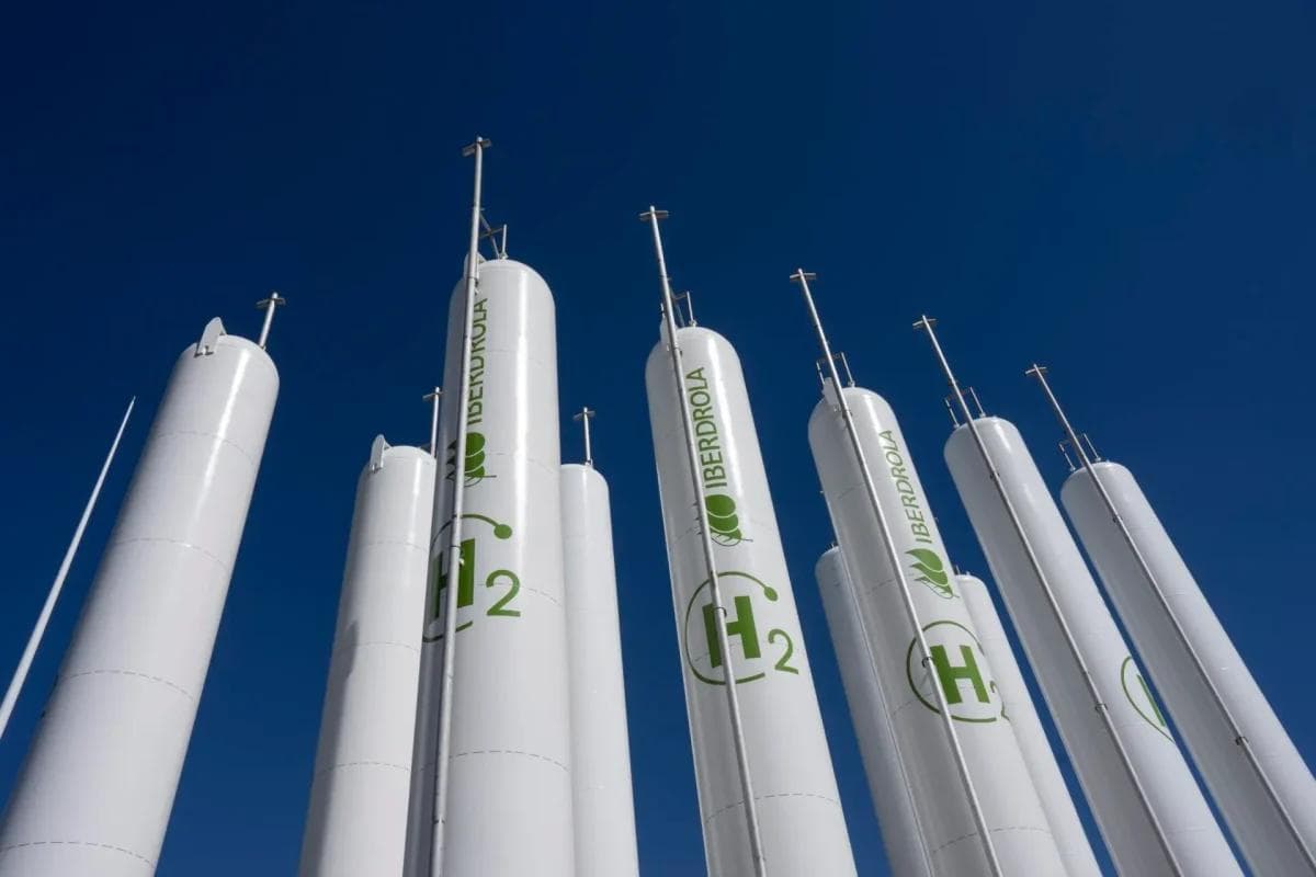 Høye hvite hydrogentanker med «Iberdrola»-logoer og «H₂»-symboler står mot en klar blå himmel.