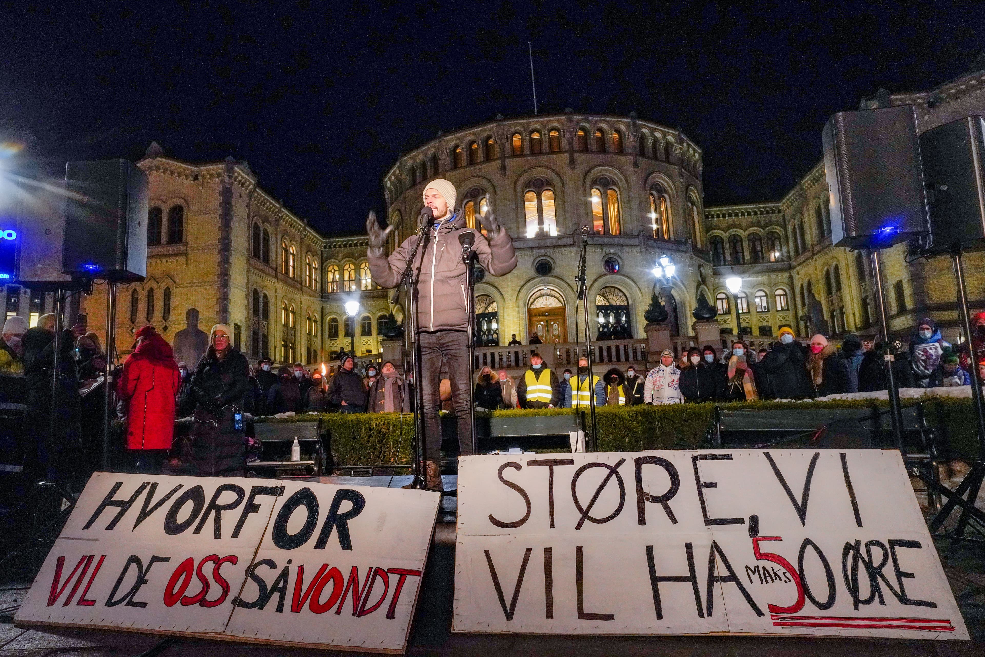 En mann holder en appell utenfor Stortinget, med to norske protestplakater i forgrunnen. På plakatene står det: Hvorfor vil de oss så vondt? Og: Støre, vi vil ha 50 øre.