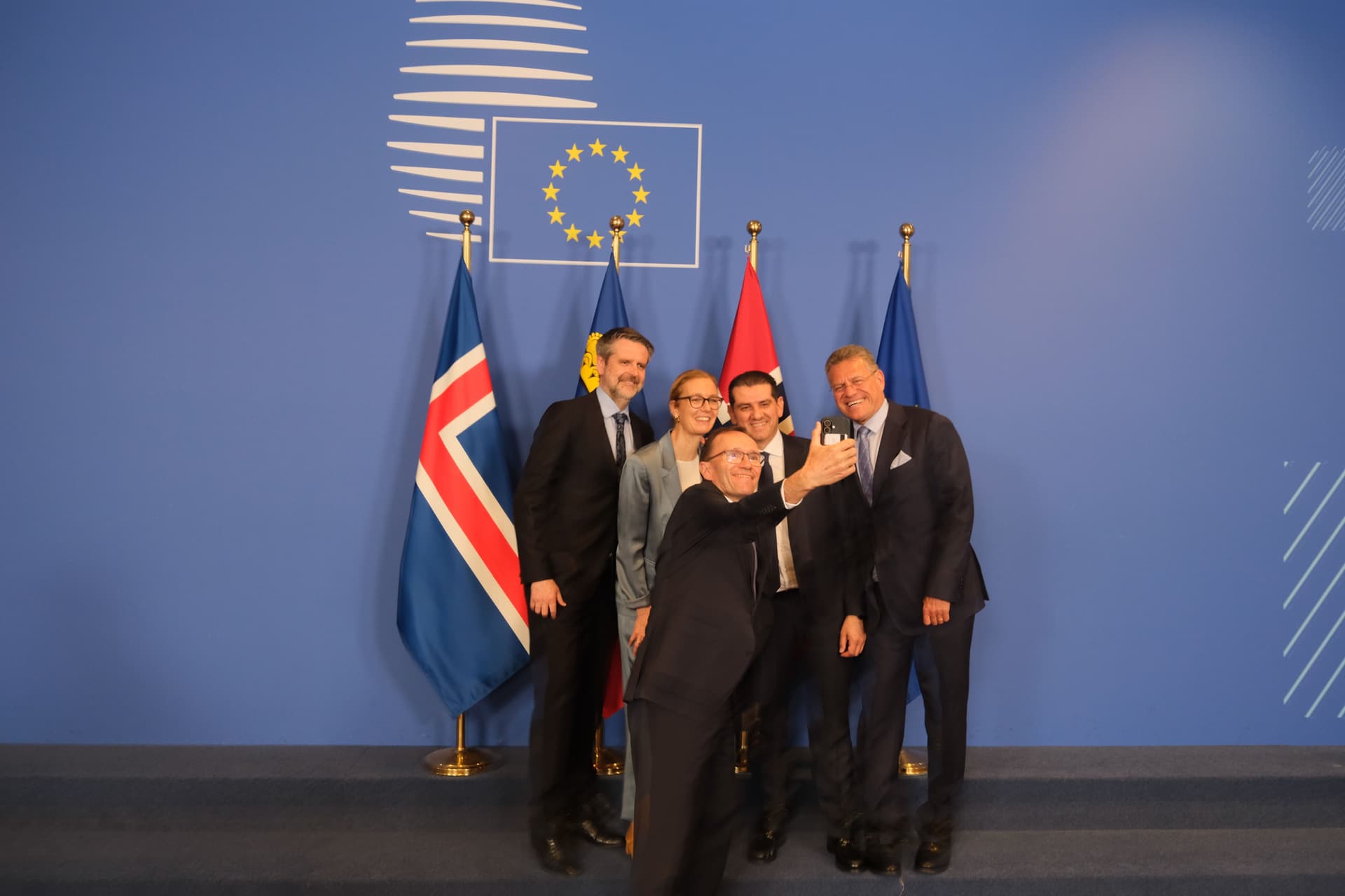 Fem smilende personer tar en selfie foran EU- og nasjonalflagg, blant annet Islands flagg.