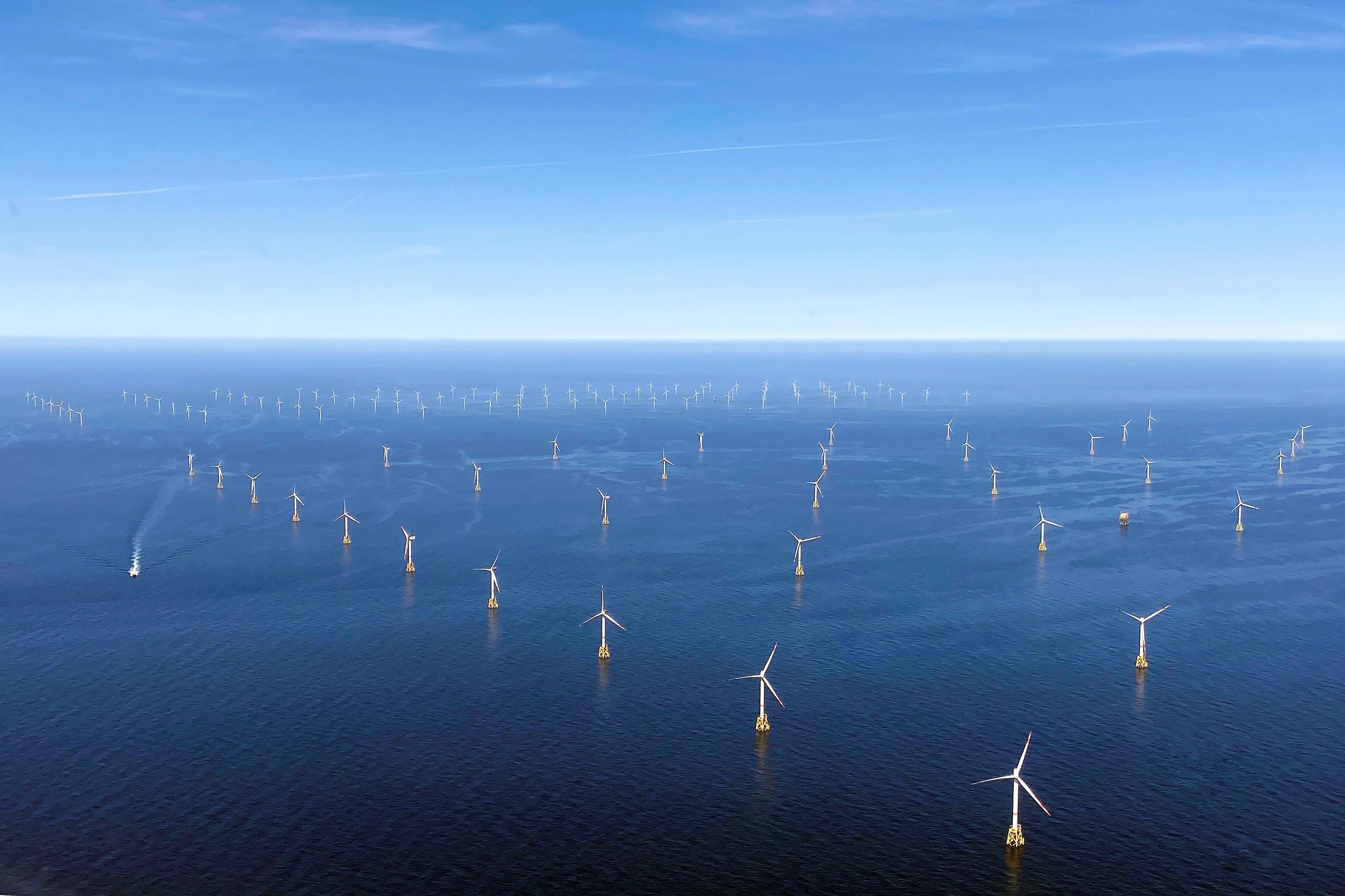 Havvindpark med en rekke turbiner i havet under blå himmel.