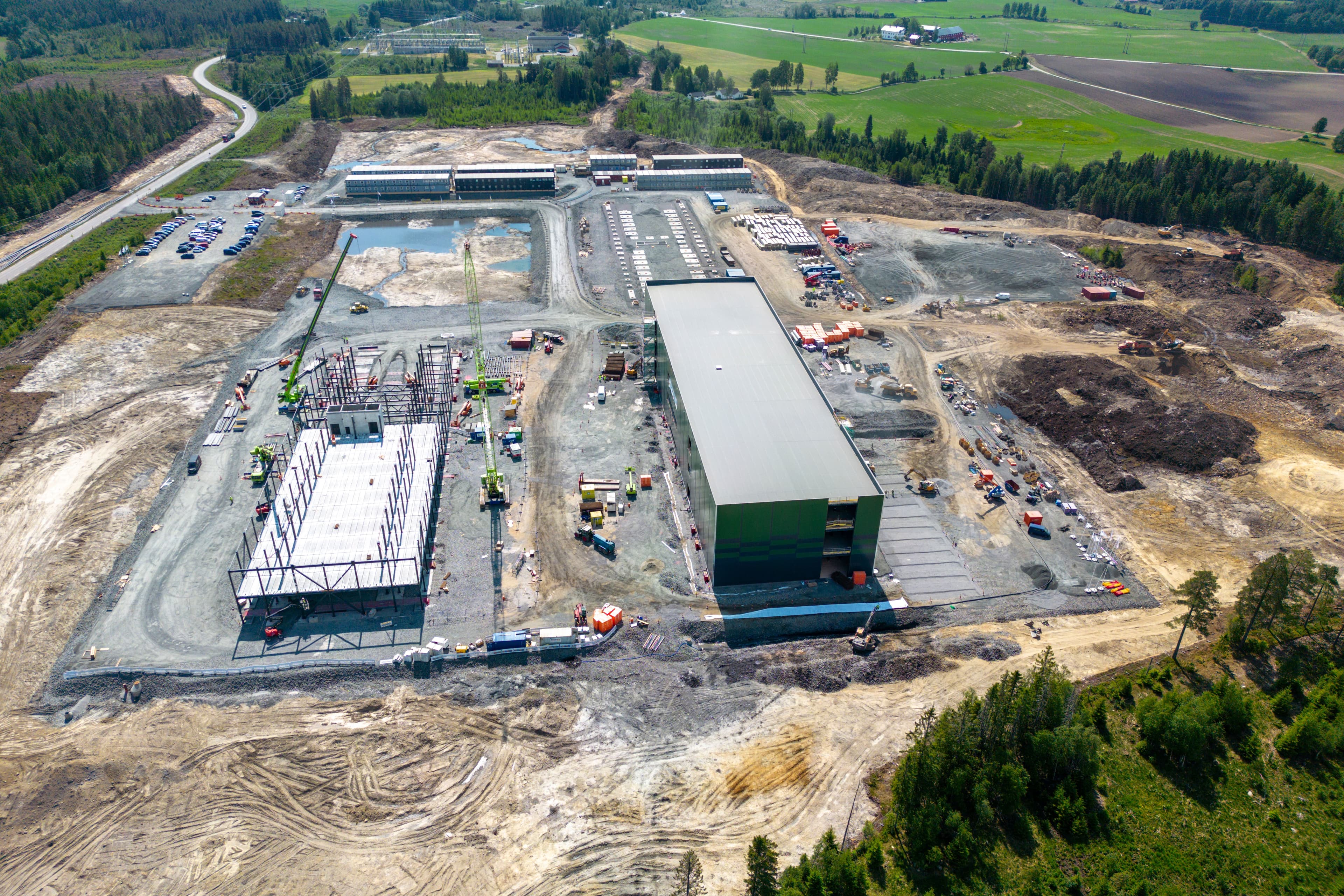 Stort industrielt anleggsområde med delvis oppførte bygg, kraner og ryddet tomt omgitt av grønne skoger.