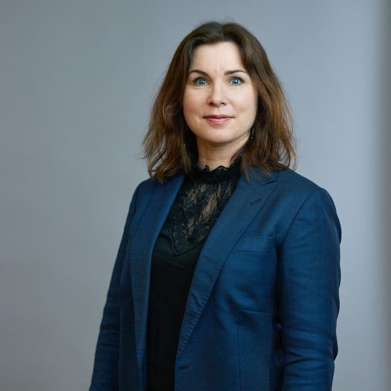 Kvinne i blå blazer står mot en grå bakgrunn, vendt fremover med et nøytralt uttrykk.