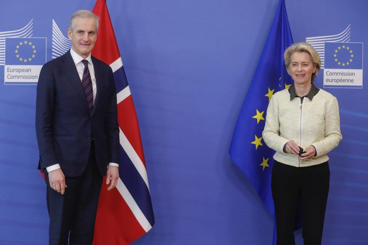 To tjenestemenn står foran norske og EU-flagg, med skilt fra Europakommisjonen synlig i bakgrunnen.