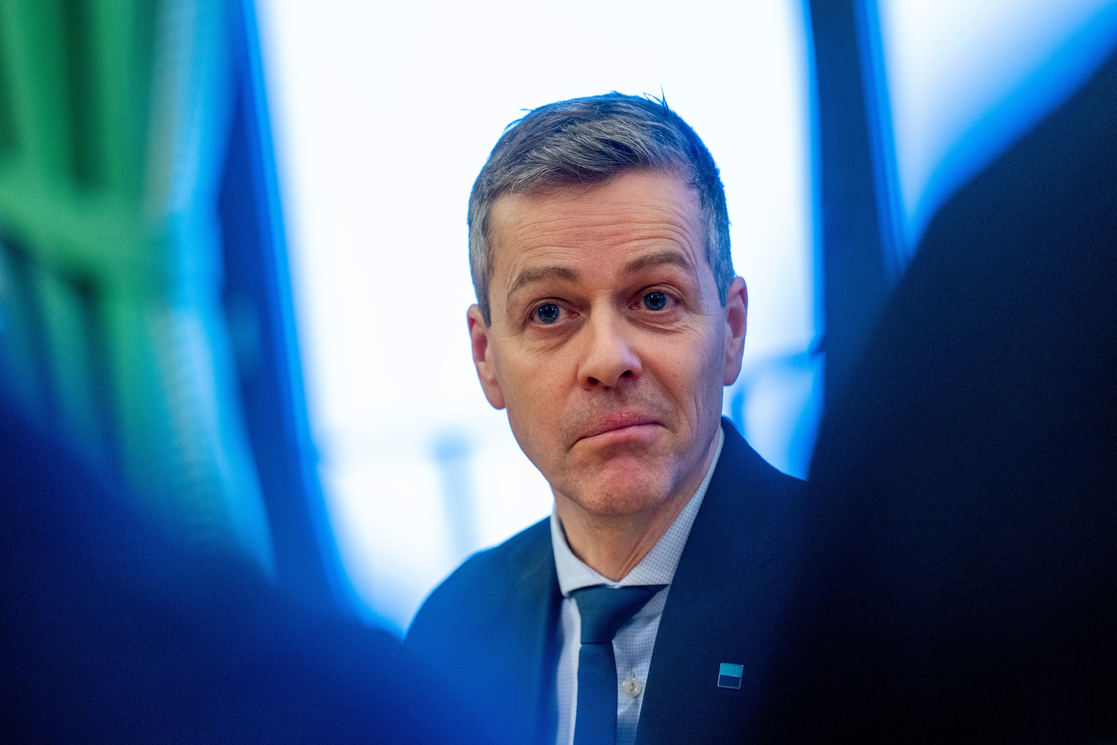 En mann med grått hår i mørk dress og blått slips ser alvorlig ut.