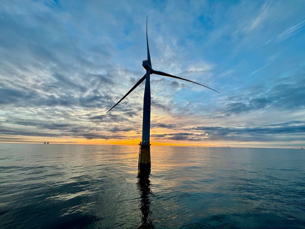 An offshore wind turbine silhouetted against a cloudy sunset over the ocean.