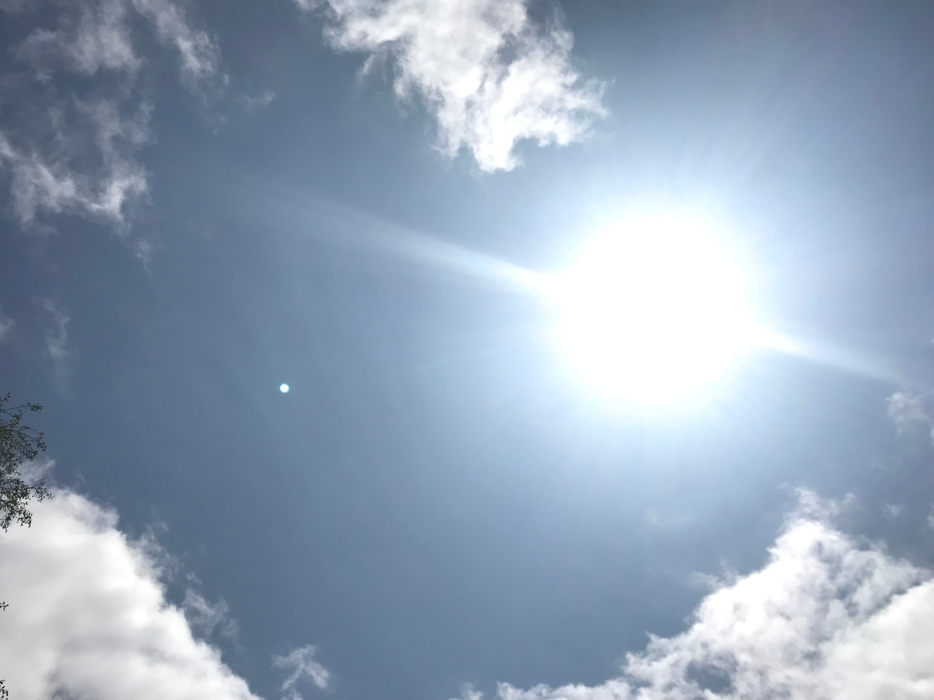 Sterk sol og linseeffekt på en blå himmel med spredte skyer.