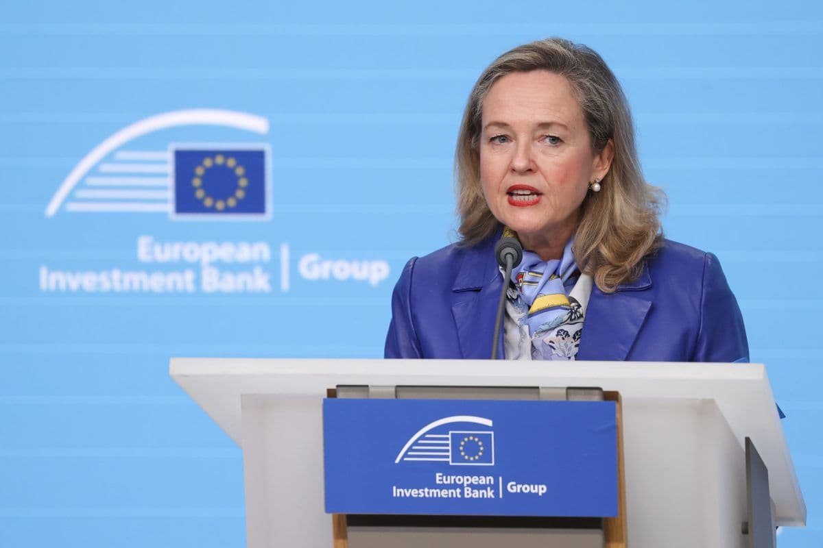 En kvinne står på et podium med Den europeiske investeringsbankens logo, snakker inn i en mikrofon, iført en blå blazer og skjerf.