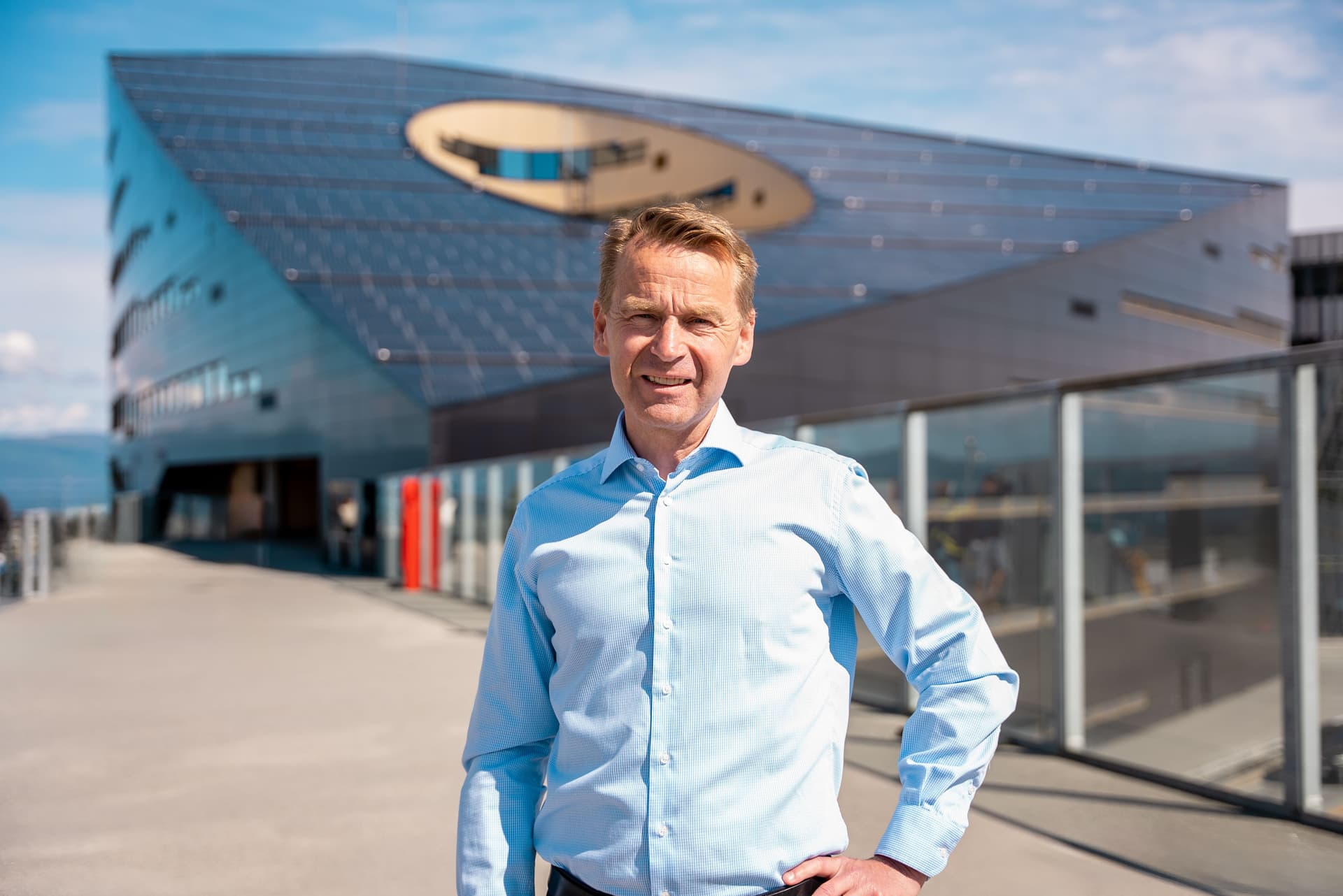 En mann i lyseblå skjorte står utendørs foran en moderne bygning dekket av solcellepaneler.