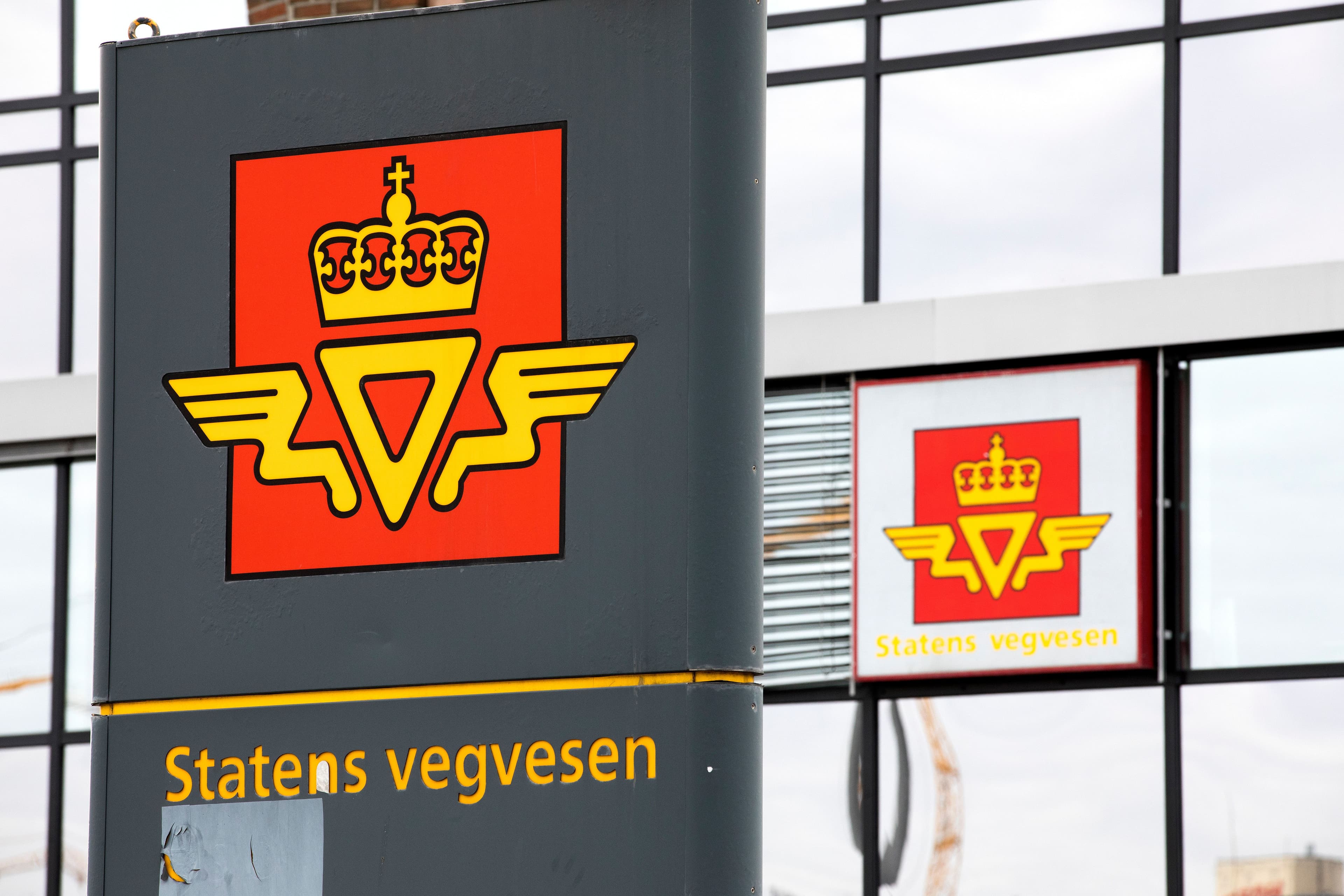 To skilt for Statens vegvesen, med en gyllen krone og en bevinget V-logo på rød, kvadratisk bakgrunn.