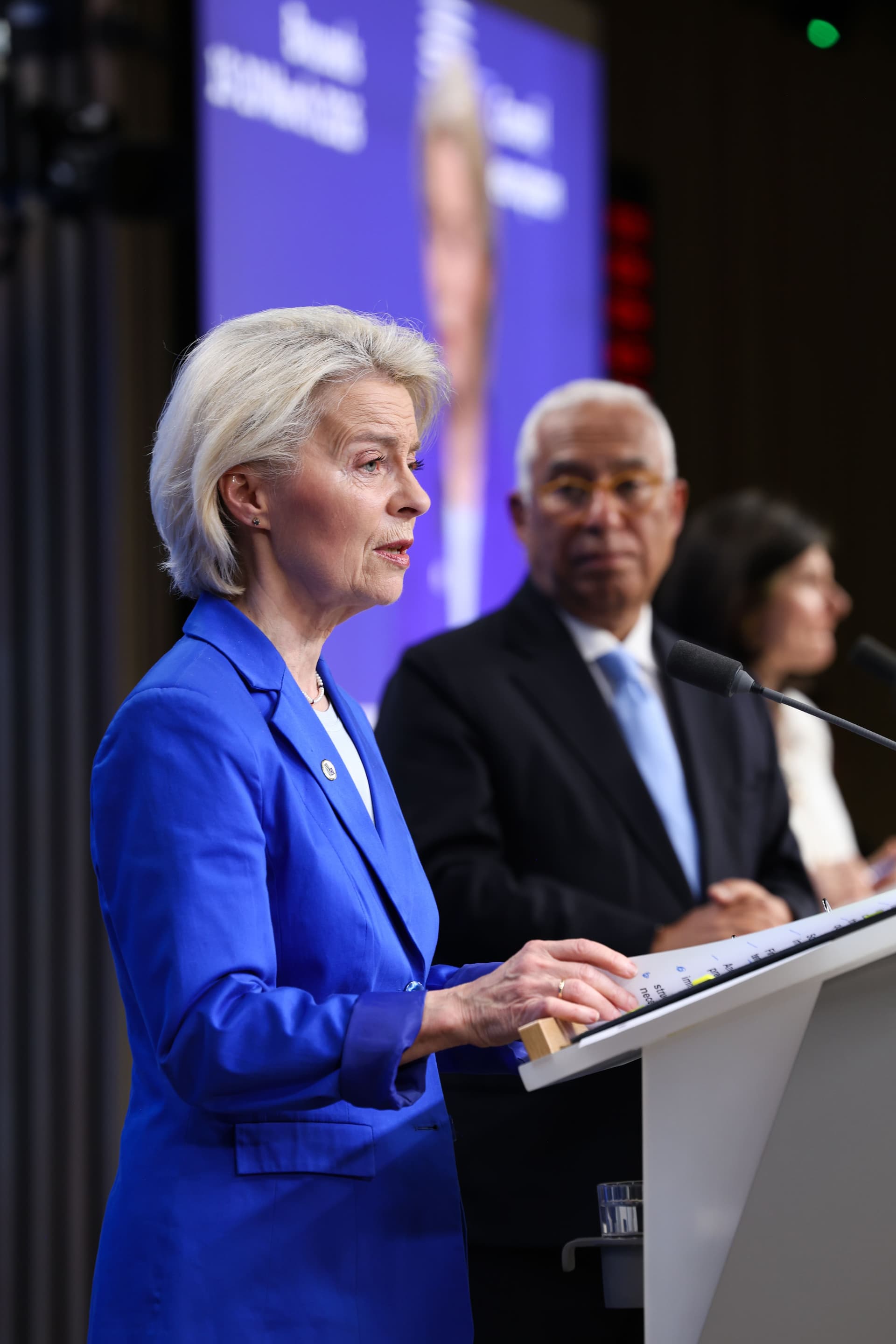 Ursula von der Leyen som taler på en pressekonferanse, med António Costa uskarp i bakgrunnen.