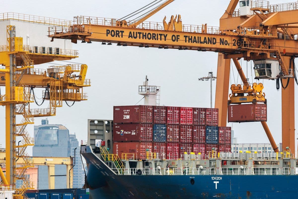 Et skip ligger til kai under en stor kran merket "Port Authority of Thailand No. 261," laster eller losser røde fraktcontainere.
