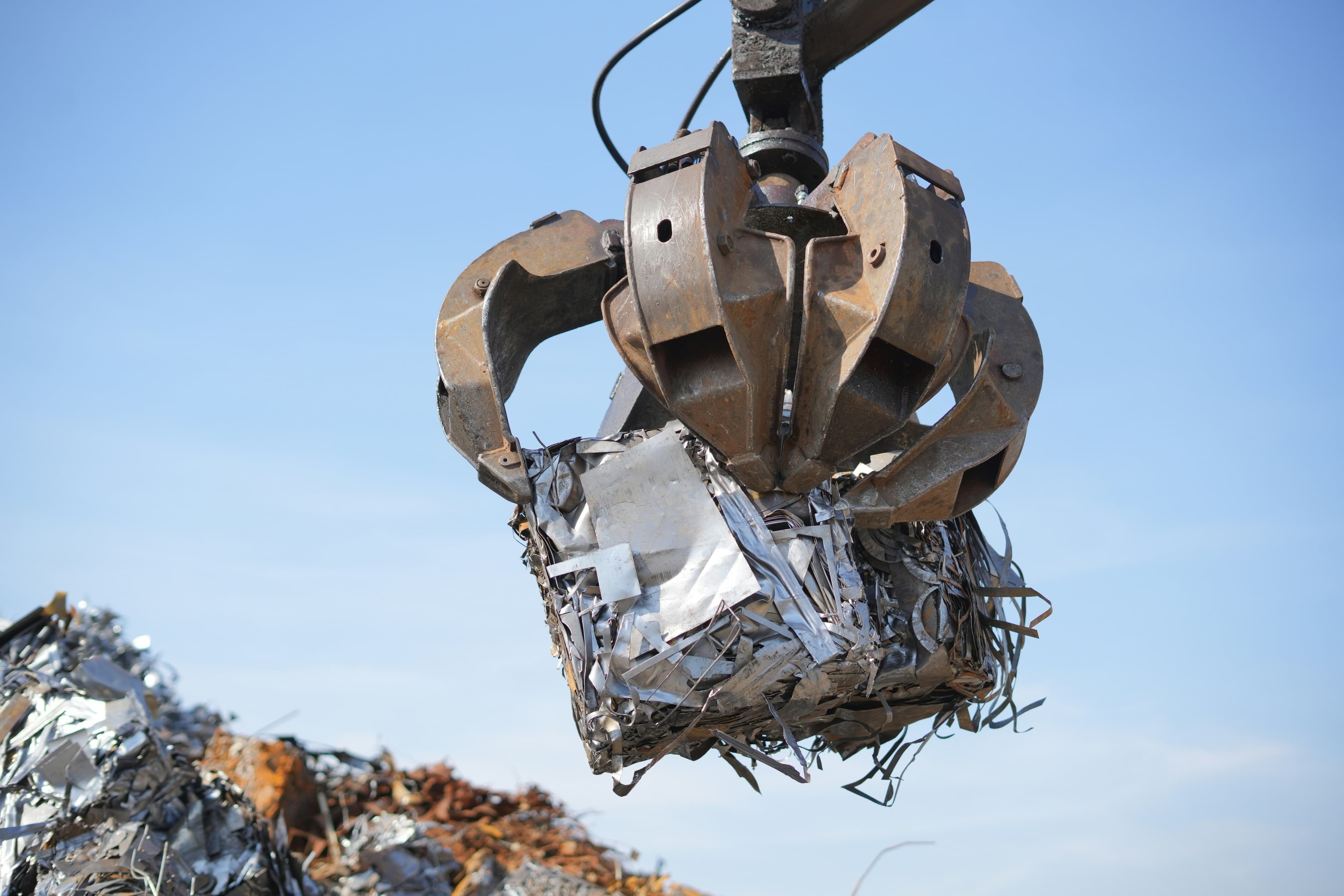 A large grapple holds a cube of compacted metal scrap.