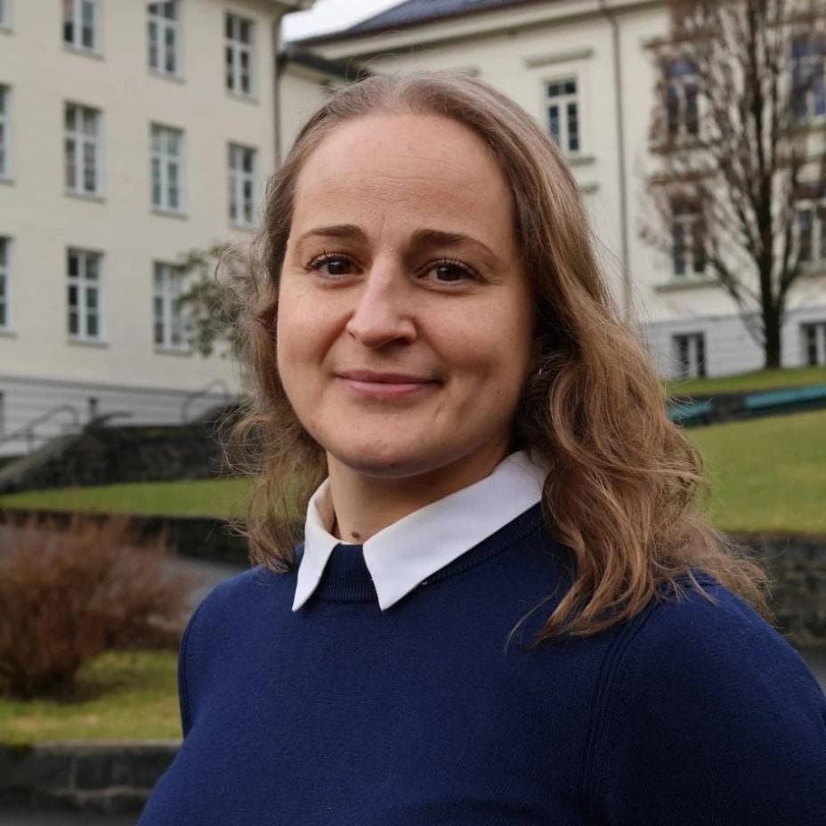 En smilende kvinne som har på seg en marineblå genser med hvit krage utendørs.