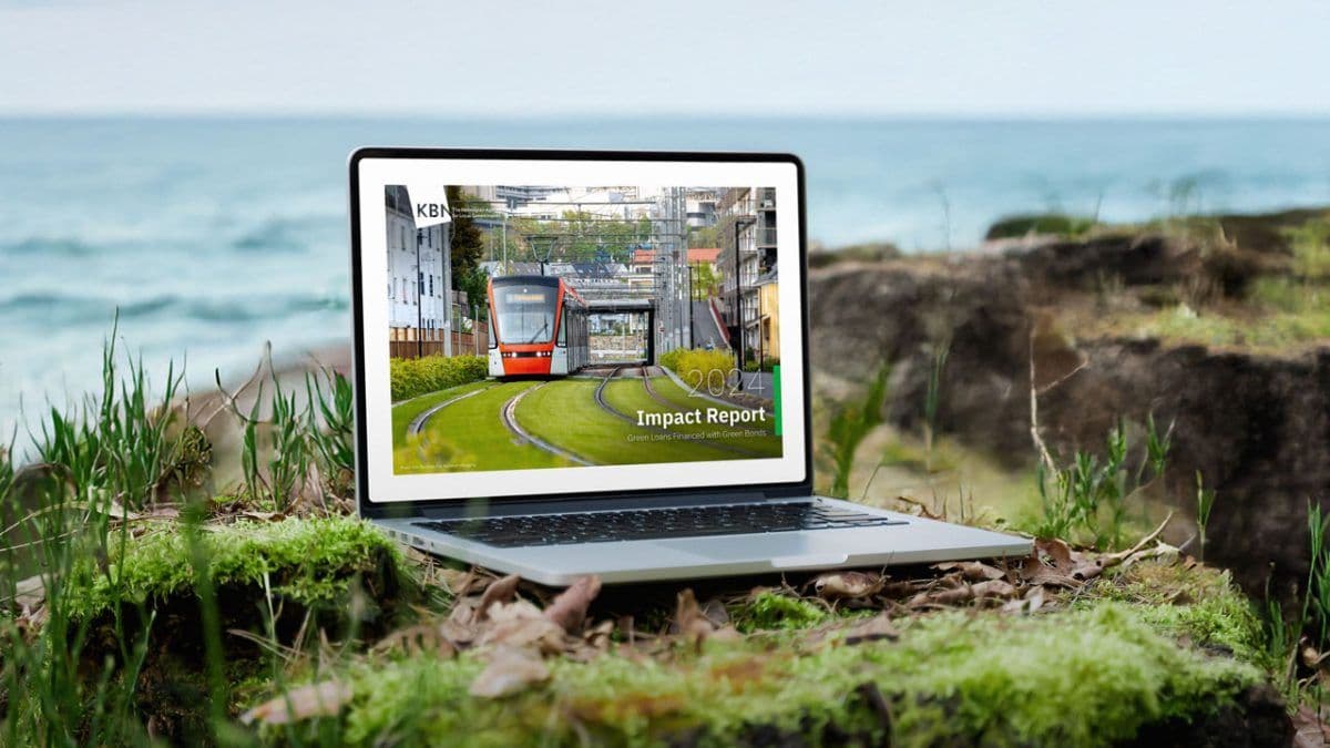 En bærbar datamaskin som viser en "Impact Report" med et trikkebilde på skjermen er plassert på gress ved en steinete strandlinje.