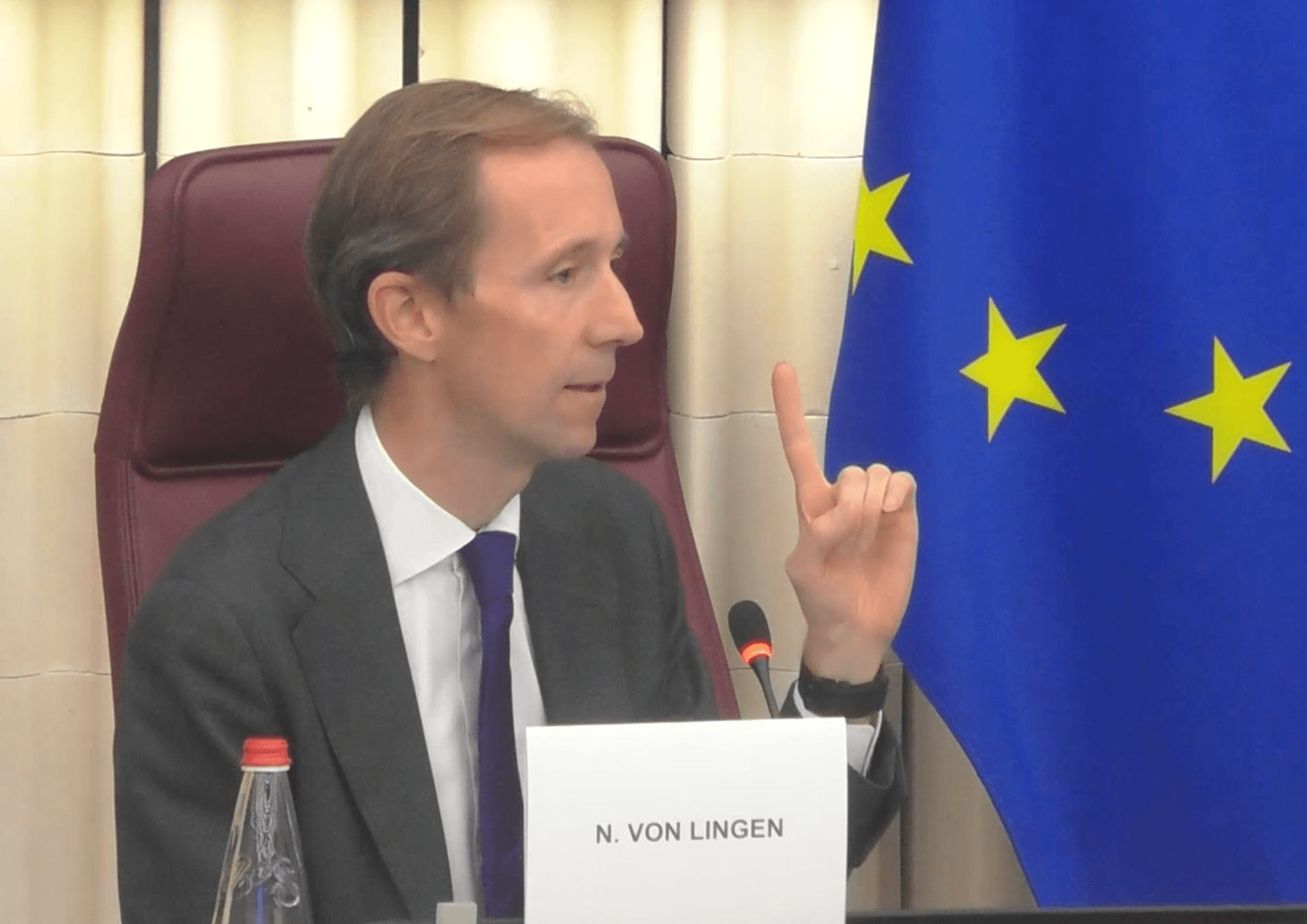 N. von Lingen speaking and gesturing with an index finger, with an EU flag in the background.
