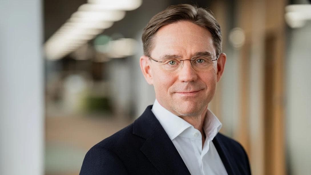 Portrettfoto av en mann i dress og briller som smiler svakt.